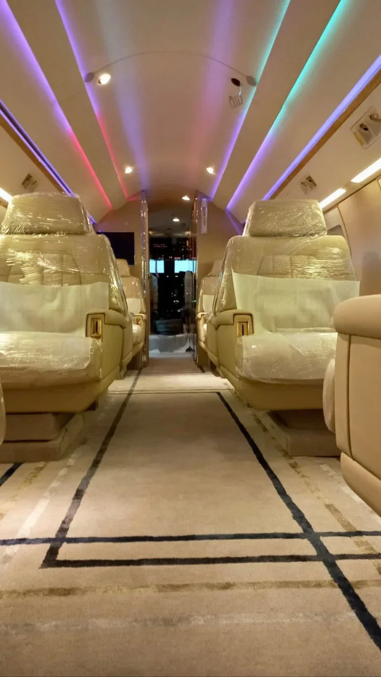 Intérieur d'un avion avec des sièges en cuir beige emballés et un éclairage LED multicolore au plafond.