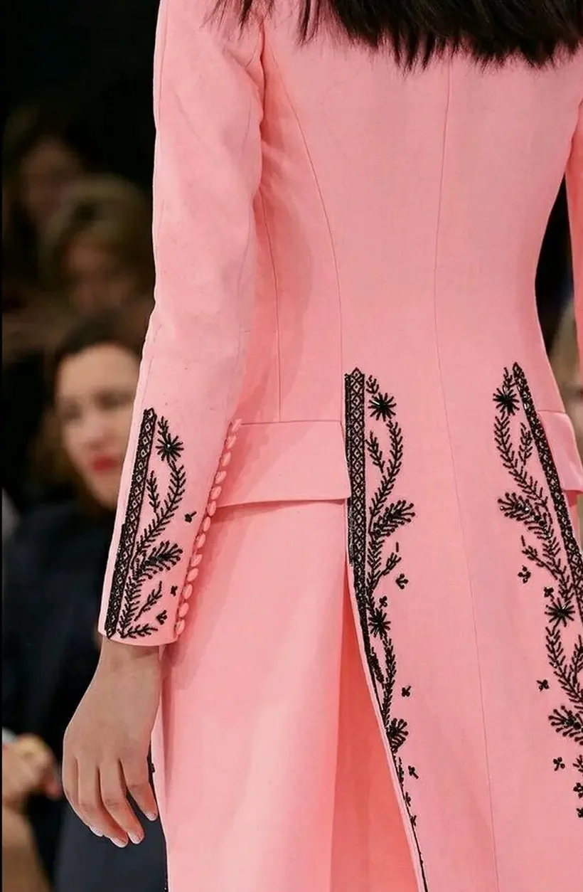 Veste ou robe rose avec broderies noires de motifs floraux et de feuilles. Manche longue, bouton sur le poignet, coussinet et taille cintrée.