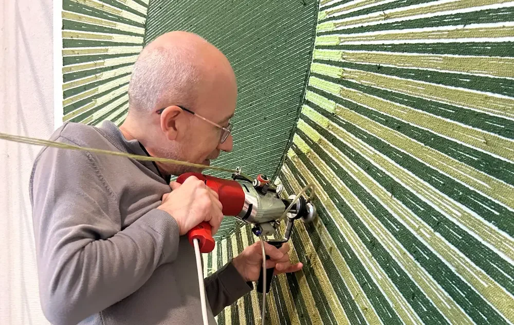A rug depicting a man using a hand-tufted tool to work on a surface, with a striped green background.