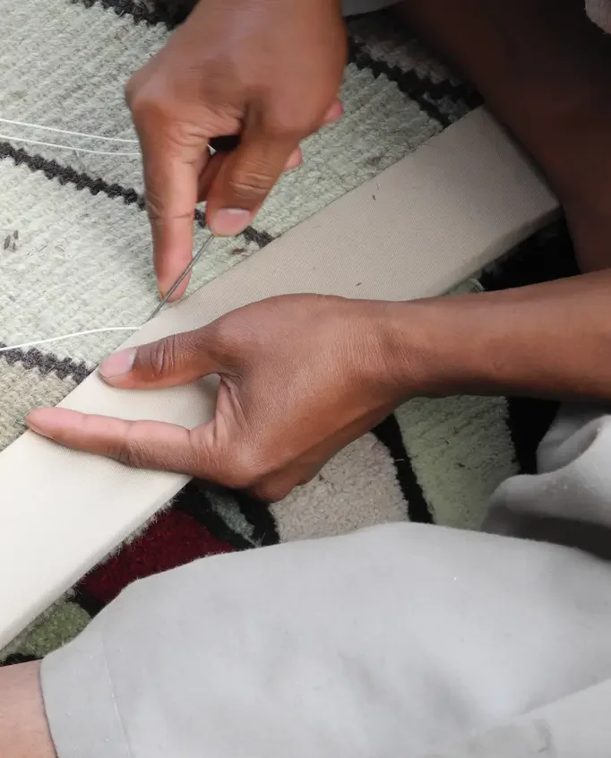 Une personne en train de coudre une pièce de tissu blanc à l'aide d'une aiguille et d'un fil, avec une main tenant le tissu et l'autre travaillant sur la couture.