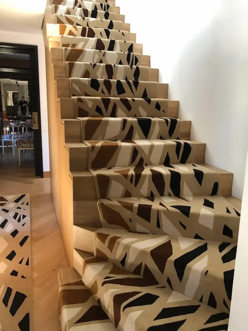 Escalier en bois avec un tapis décoratif à motifs abstraits en beige, noir et marron.