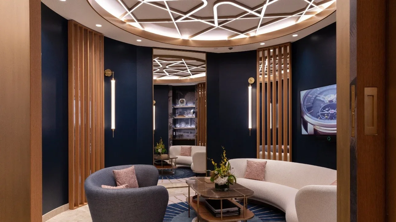 An elegant living room featuring white sofas, a grey armchair, modern décor, wall-mounted lighting, a television, and wood paneling.