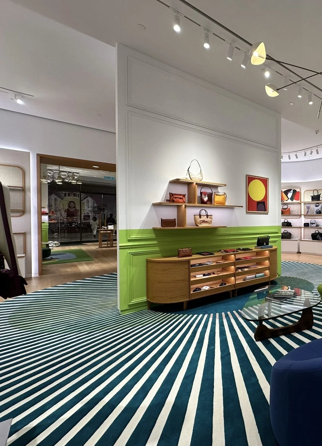 Une boutique de sacs à main avec des étagères en bois, une peinture abstraite, et un tapis rayé bleu et blanc.