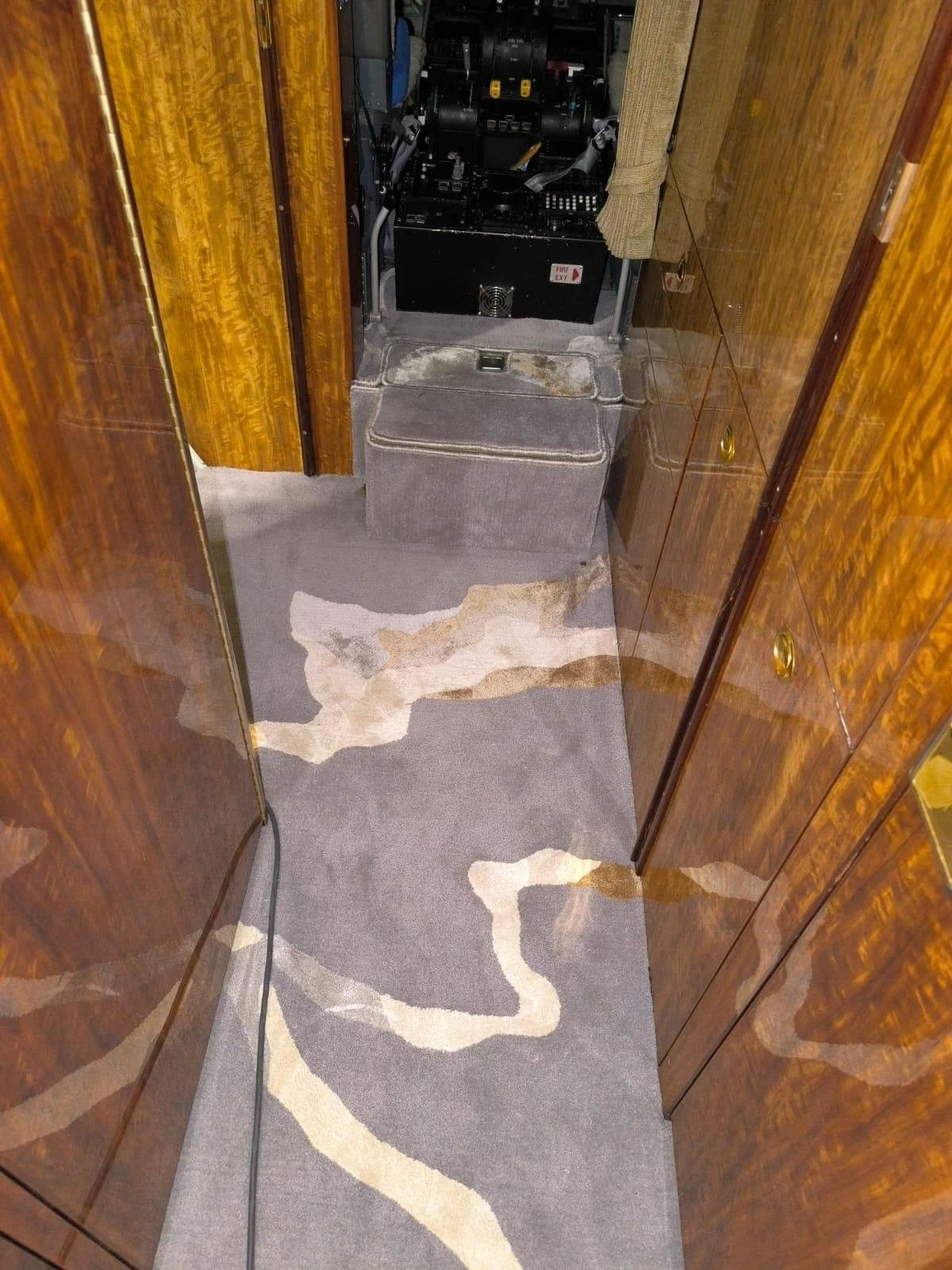 Cabine avec un tapis gris, murs en bois, un ordinateur portable fermé, un coffre en tissu, et un équipement électronique en arrière-plan.