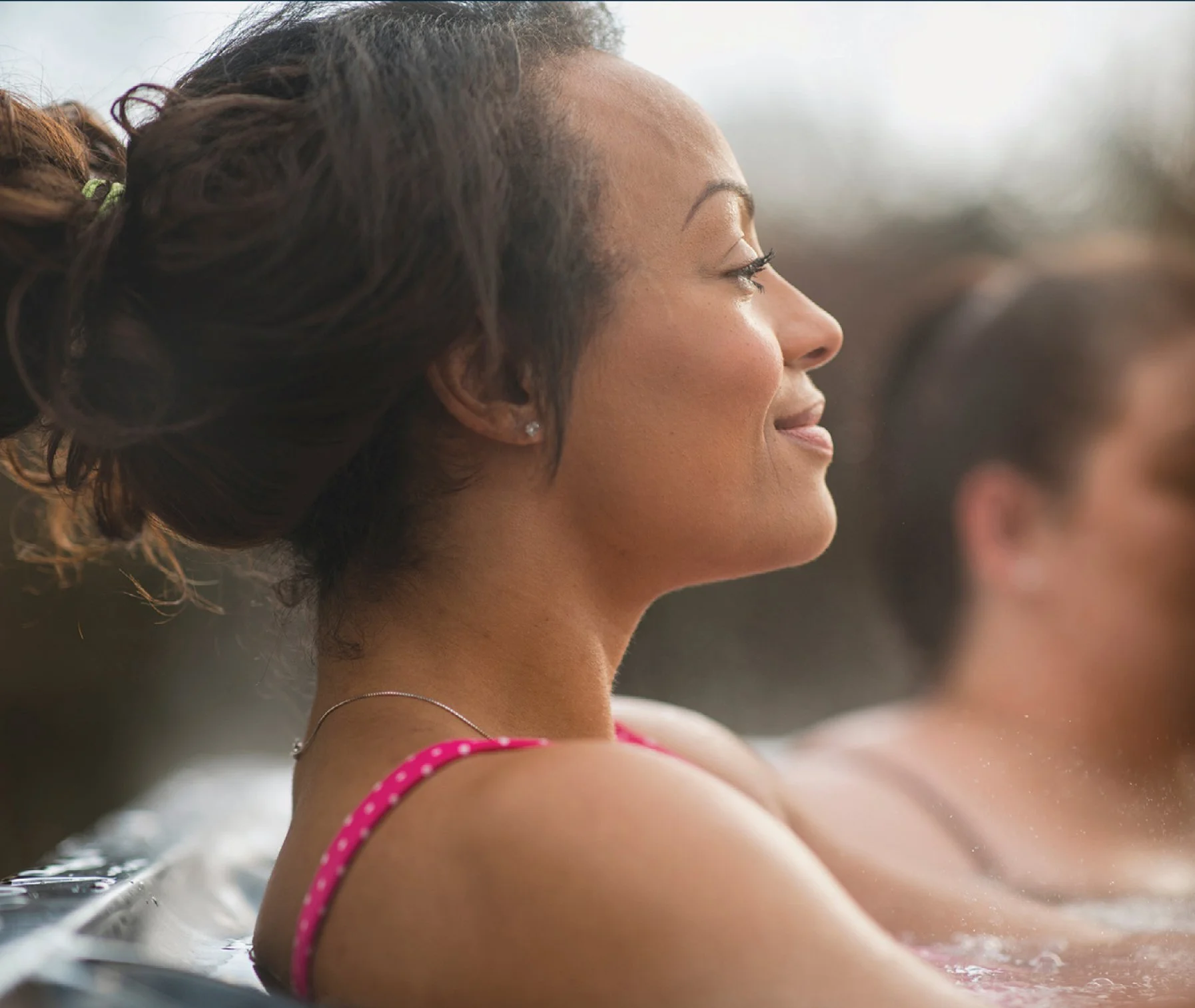 Women relaxing in a pool with serene expressions, close-up side view, water visible around her.