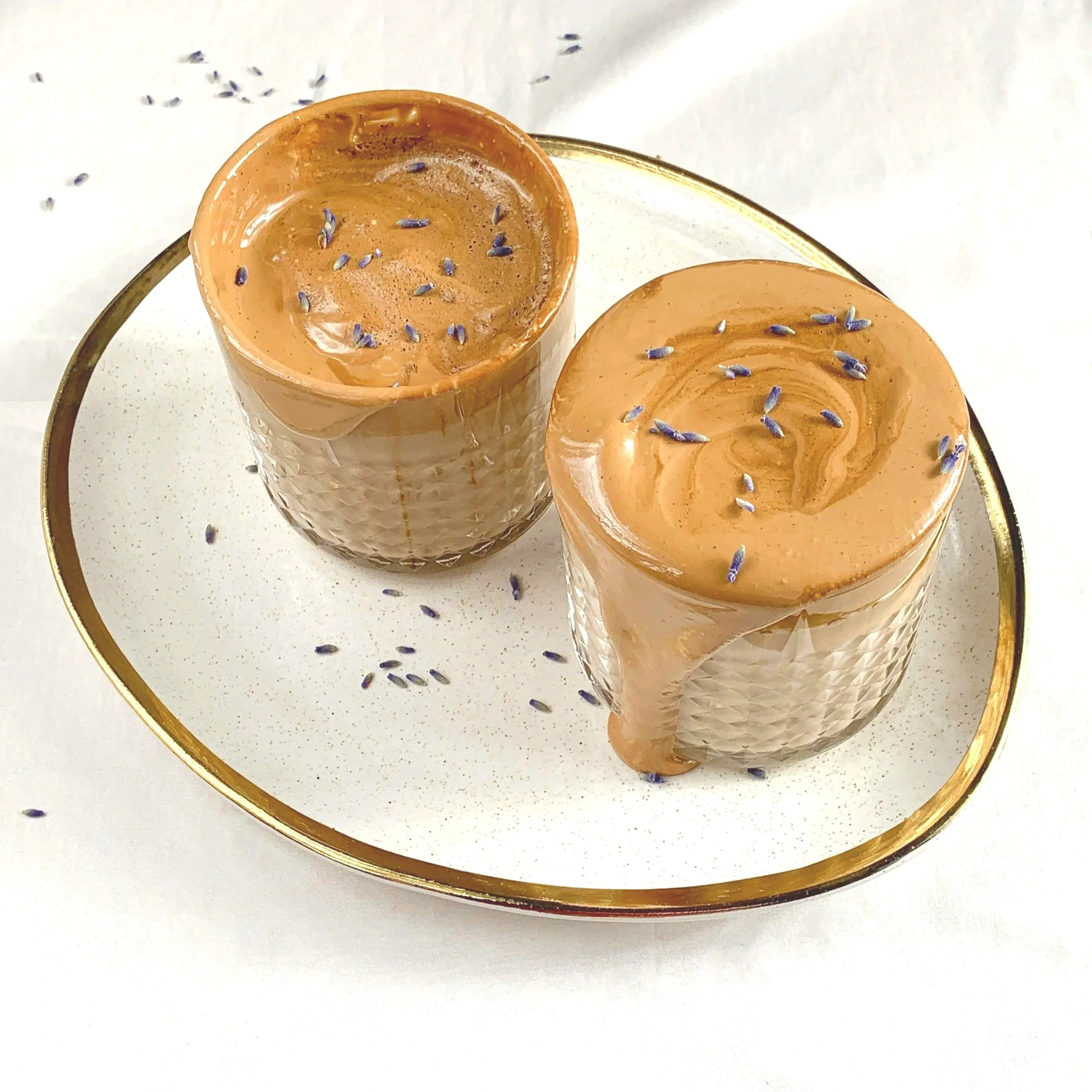 Two glasses of chai tea with crushed lavender flower sprinkles, served on a white plate with a gold rim.