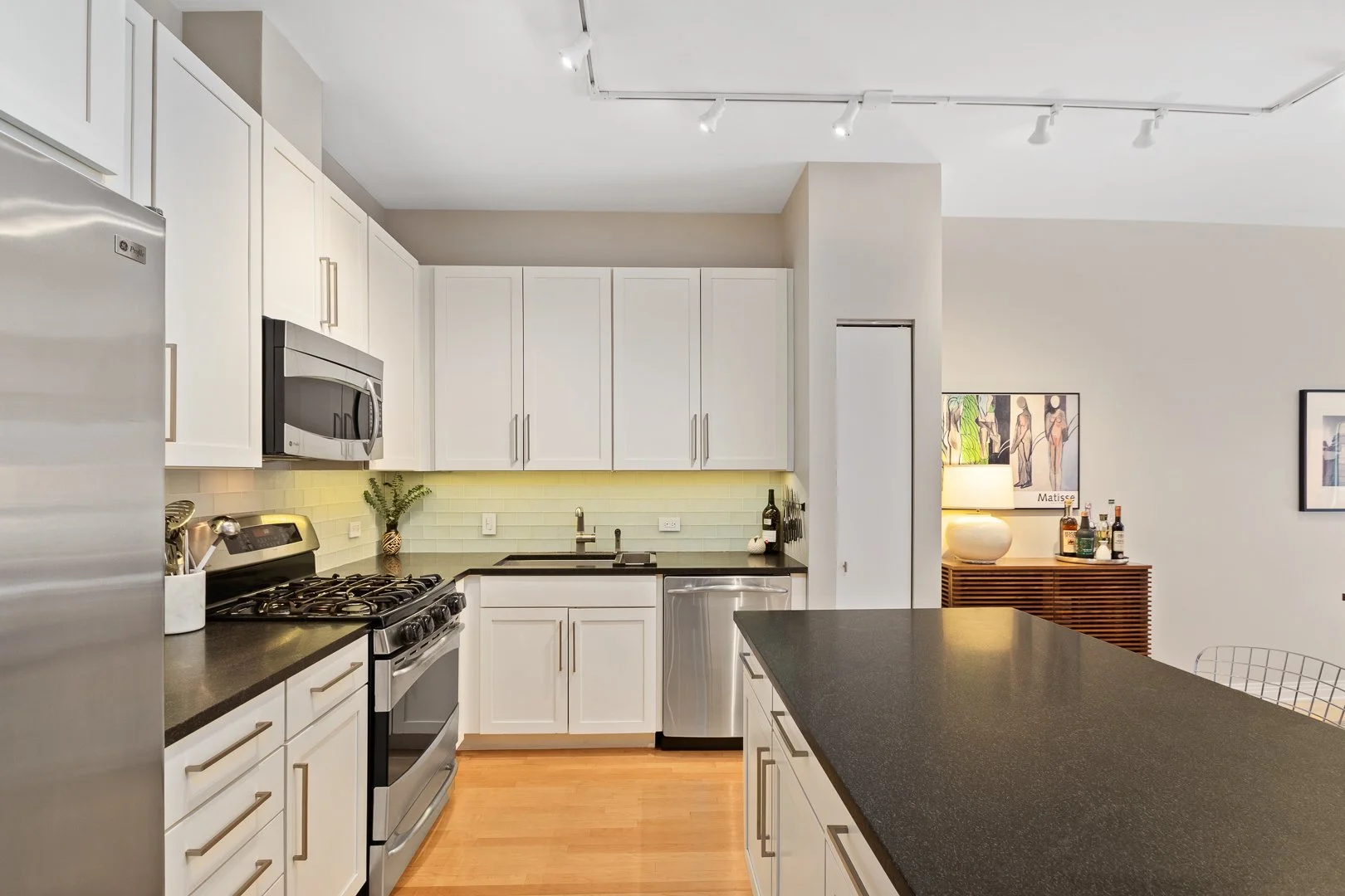Modern kitchen with white cabinets, black countertops, stainless steel appliances, and hardwood floors.