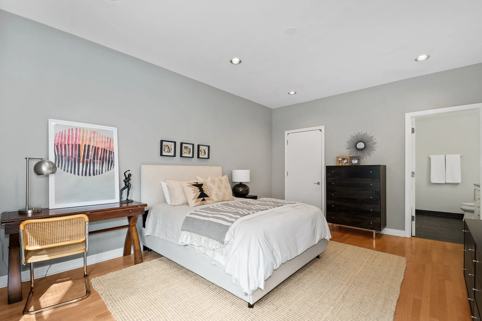 Bedroom with a white bed, black dresser, and artwork on light gray walls.