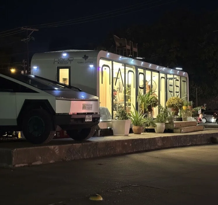 Night shot of a small mobile store called 'Armoire Test' with potted plants outside and a DeLorean car parked in front.