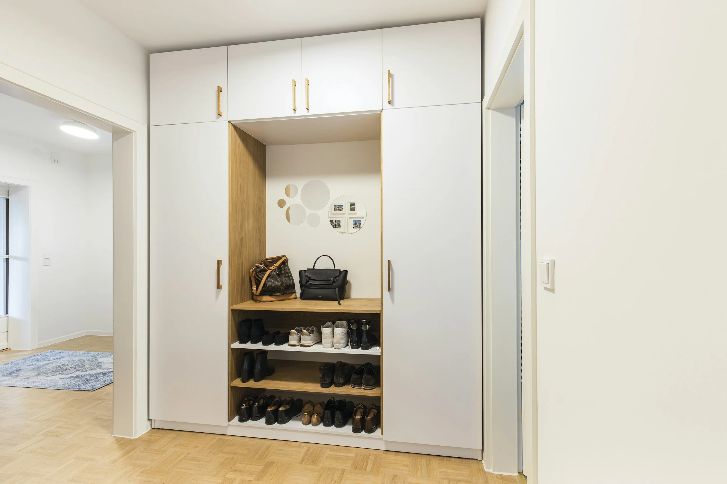 Orderly entryway closet with white cabinets and open wooden shelves filled with shoes, handbags, and small items.