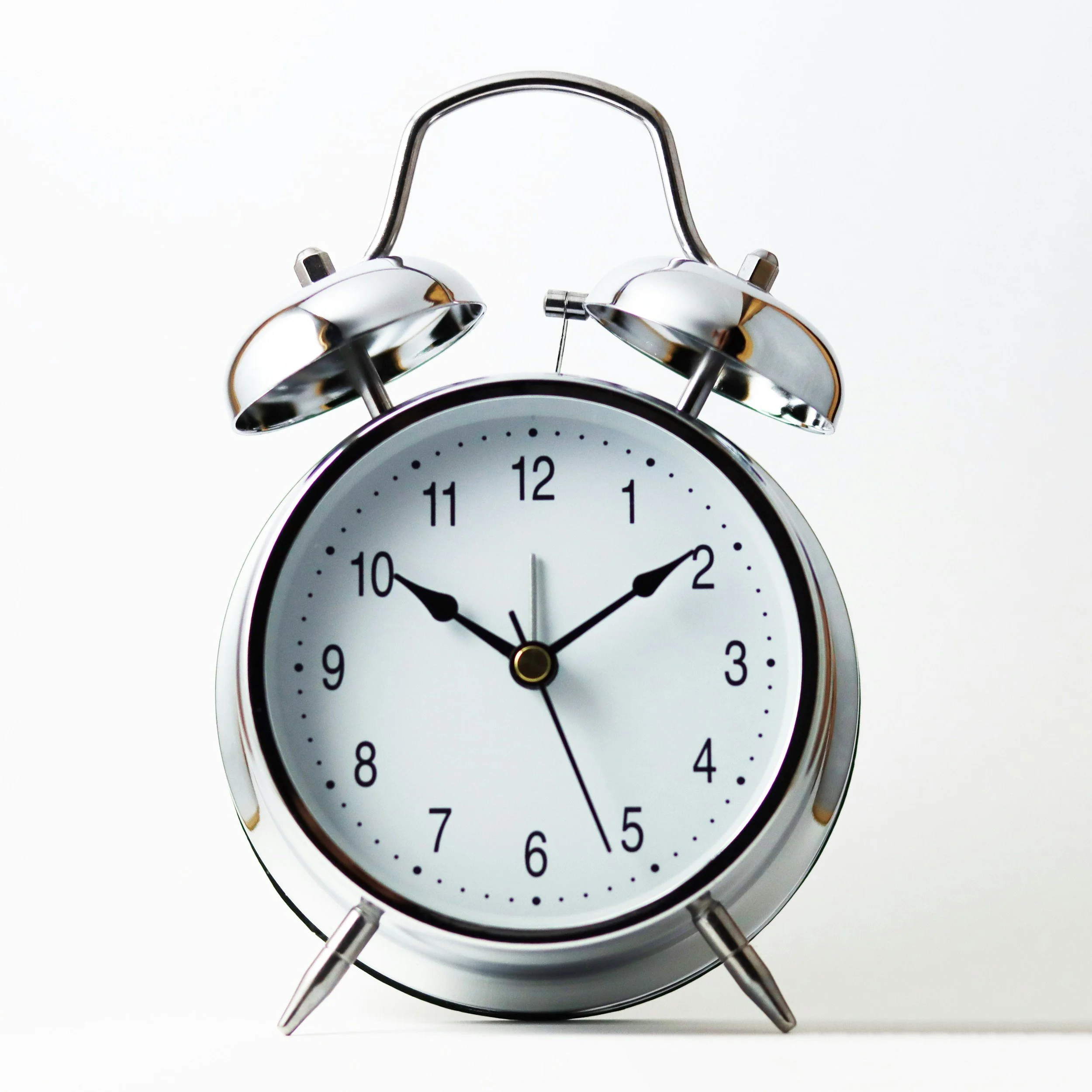 Silver vintage alarm clock showing the time as 10:09 and 26 seconds, with a white face and black hands, against a plain white background.
