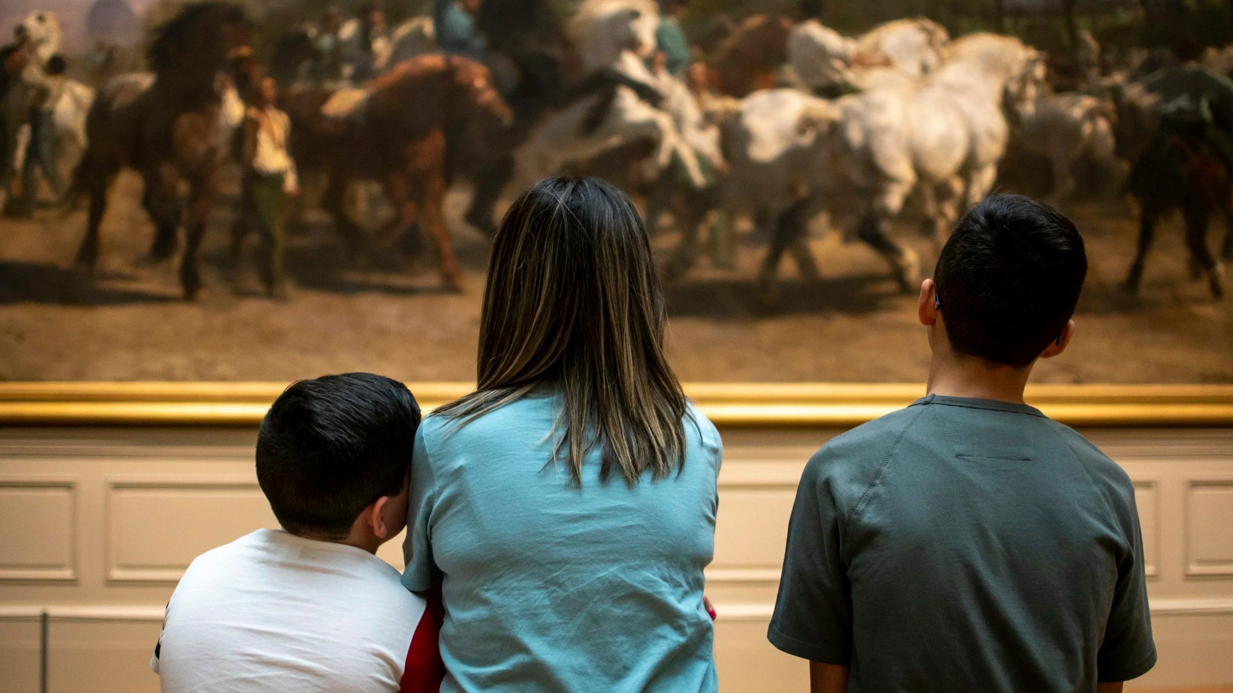 Children and a woman looking at a painting at a museum.
