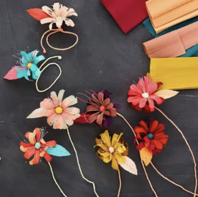 Colorful paper flower hair accessories and colored tissue paper sheets on a dark surface.