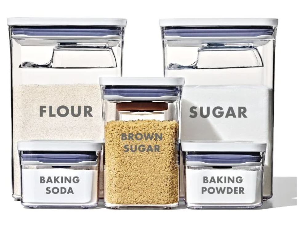 Clear storage jars labeled 'Olena's Pantry' containing frucose, buckwheat, and rice, arranged on a shelf.