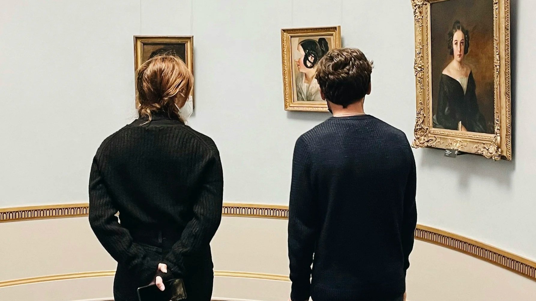 Two people, standing in an art gallery, observing paintings.