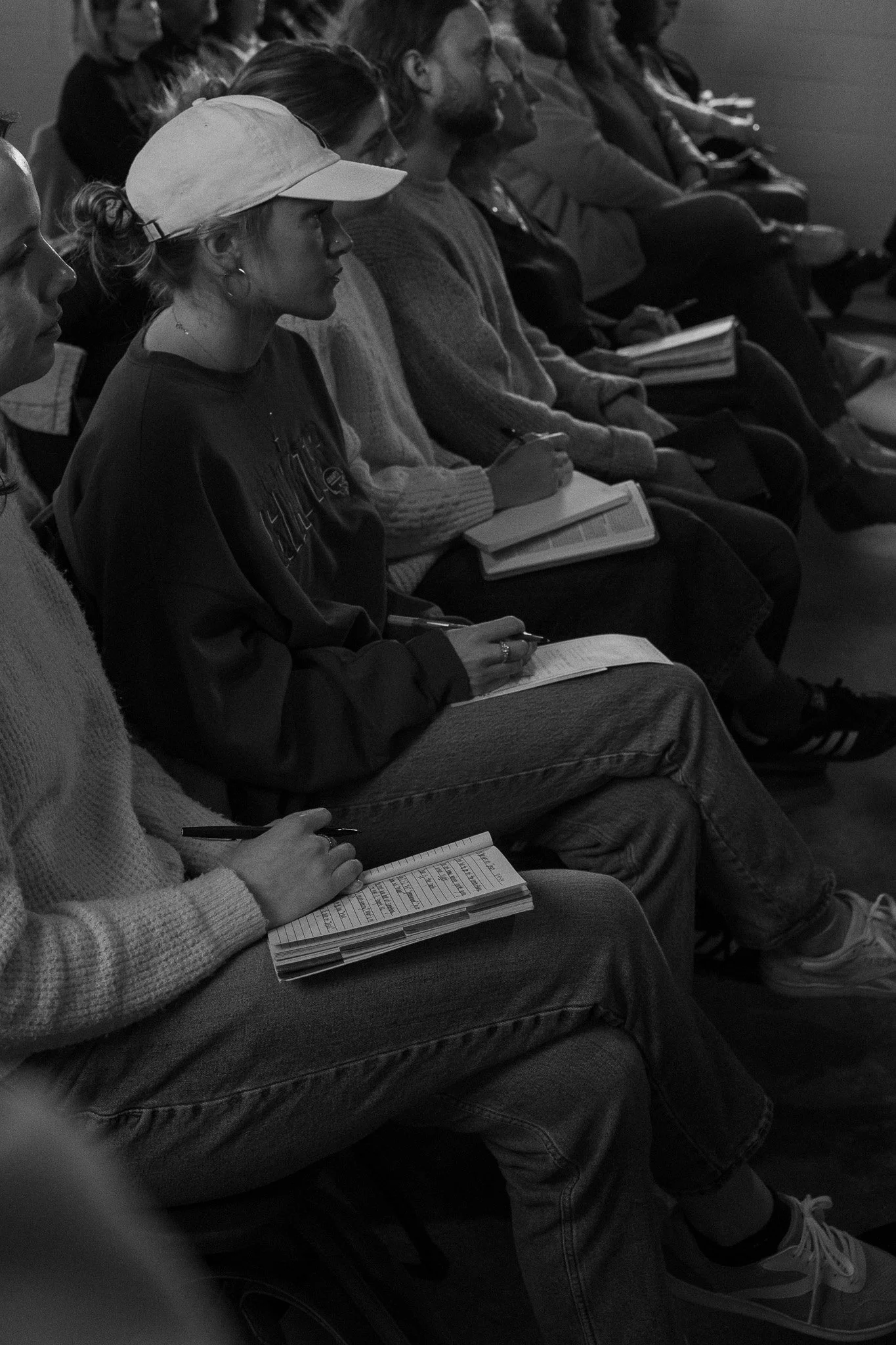 People seated in an auditorium taking notes during a lecture or presentation.