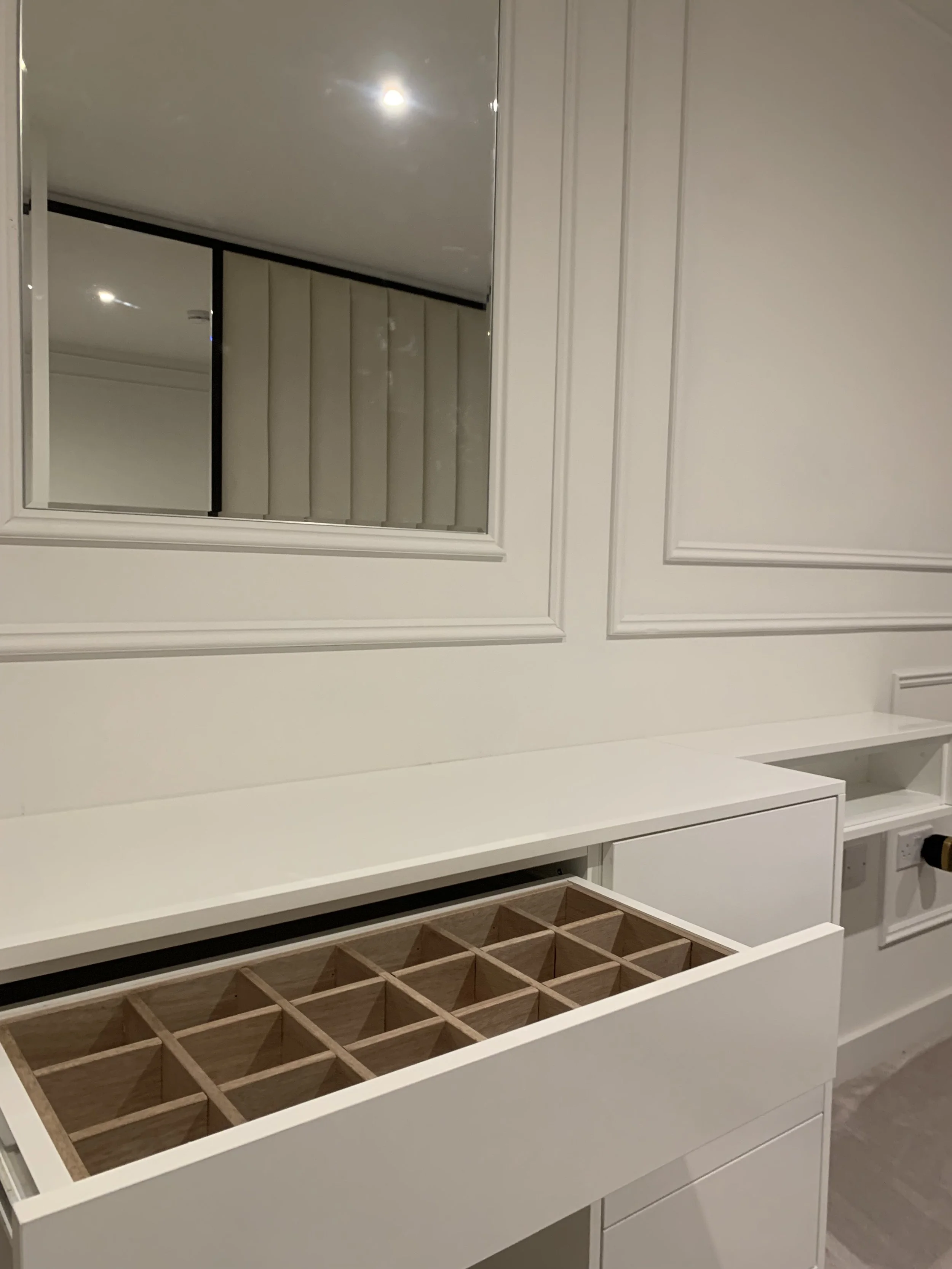 White built-in storage with a mirror, white wall paneling, and a wooden divided drawer.