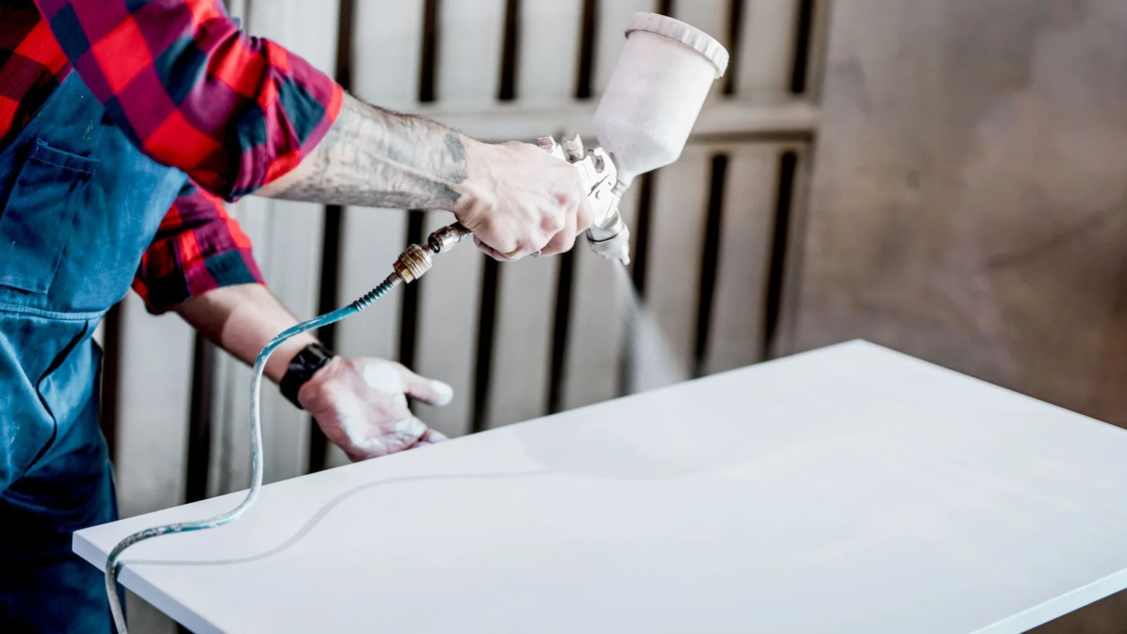 A person spray painting a white table with a spray gun in a workshop.