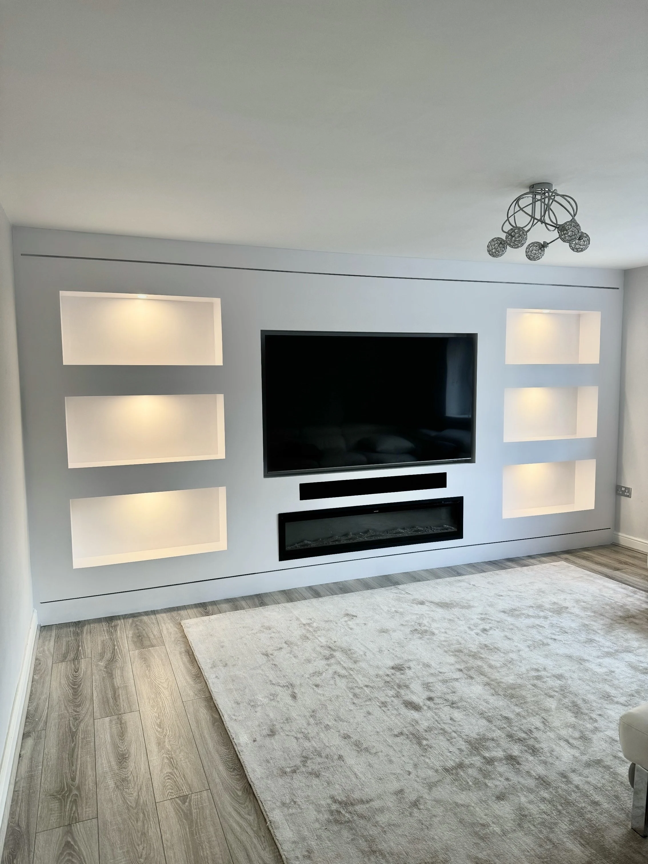 Living room wall with a large TV, floating shelf, and built-in lighting in wall niches.
