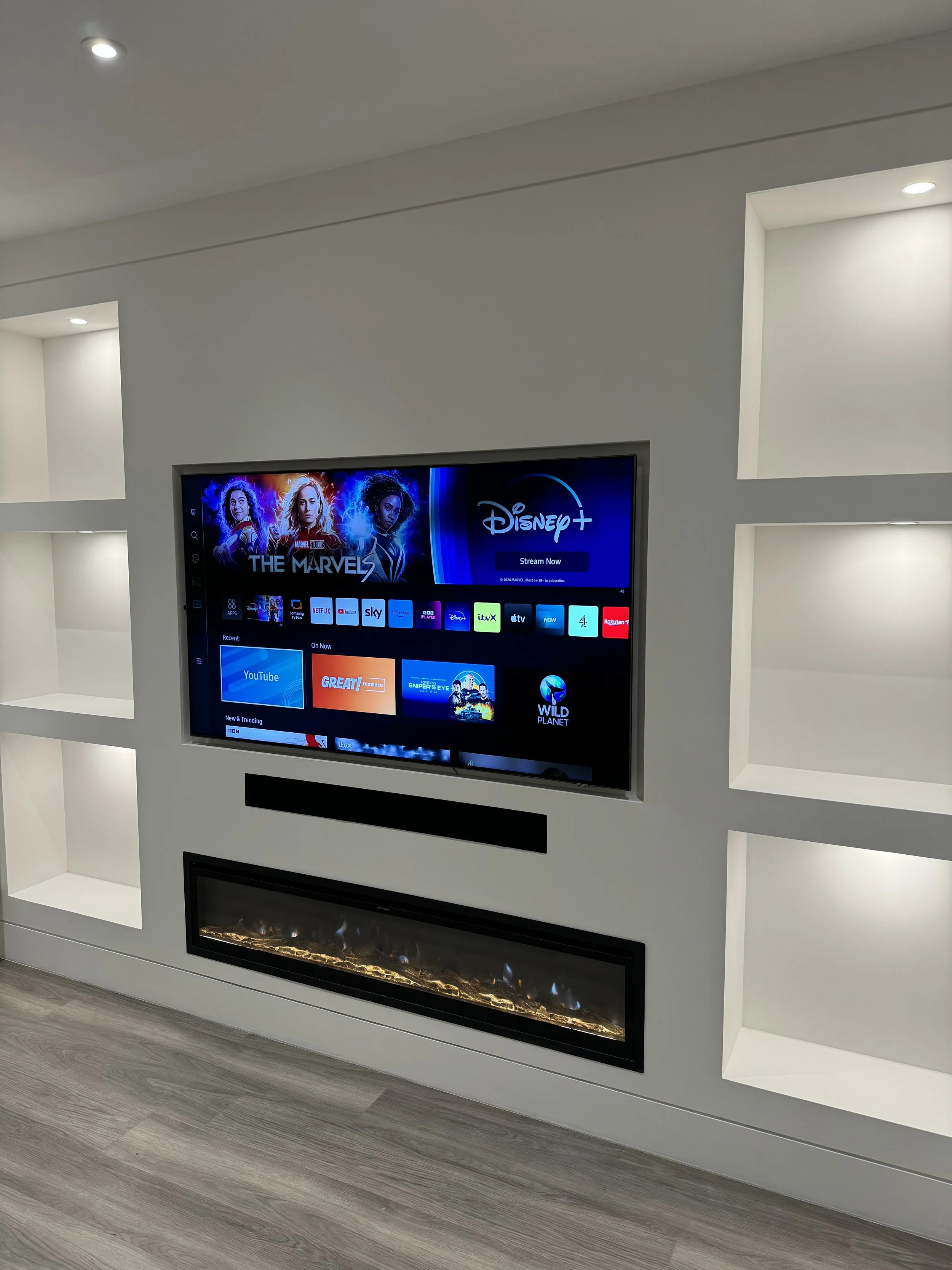 Smart TV displaying streaming content on a white wall with built-in shelves and an electric fireplace below.