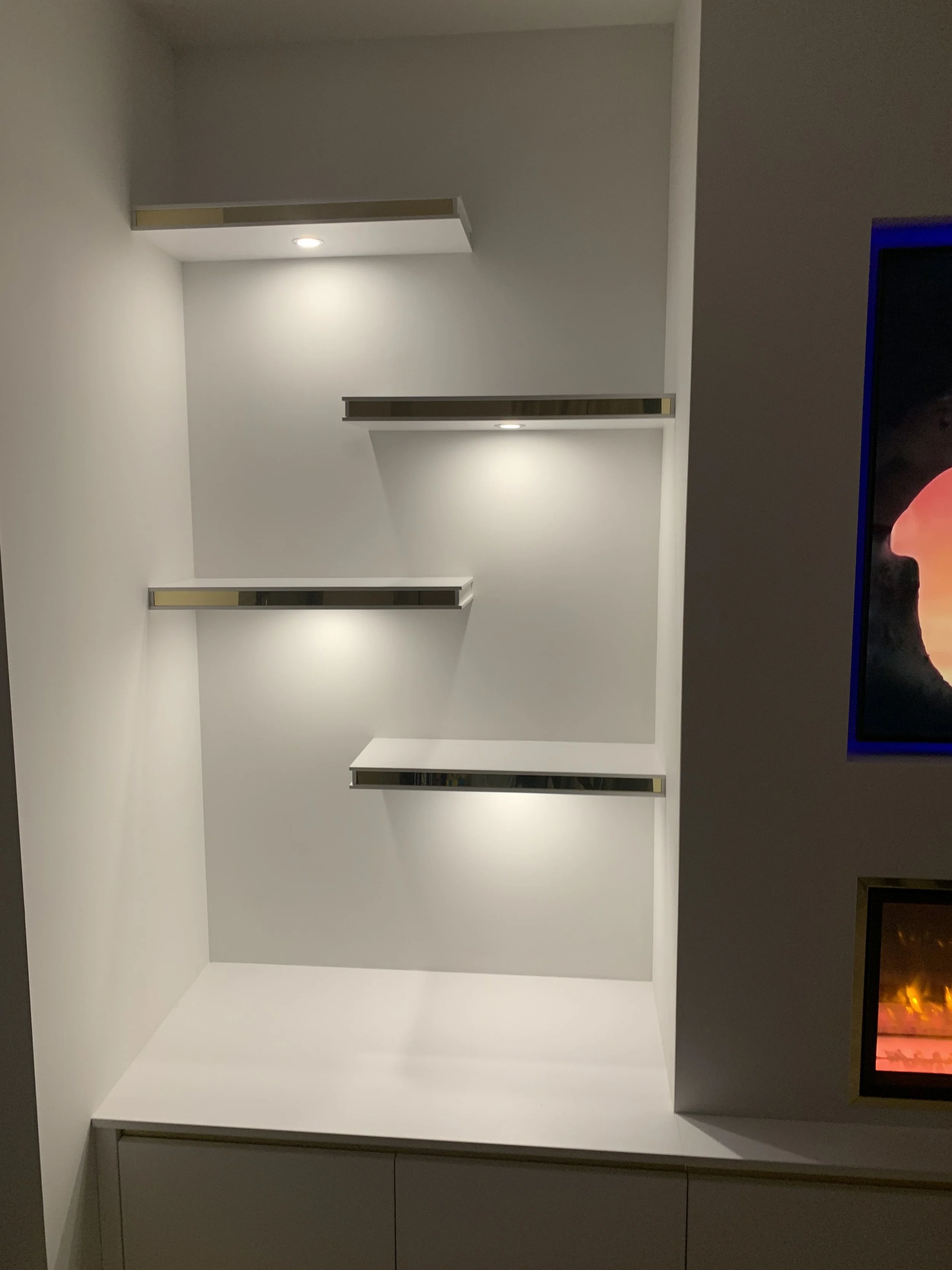 Empty white wall with four modern lights and metallic wall-mounted shelves.