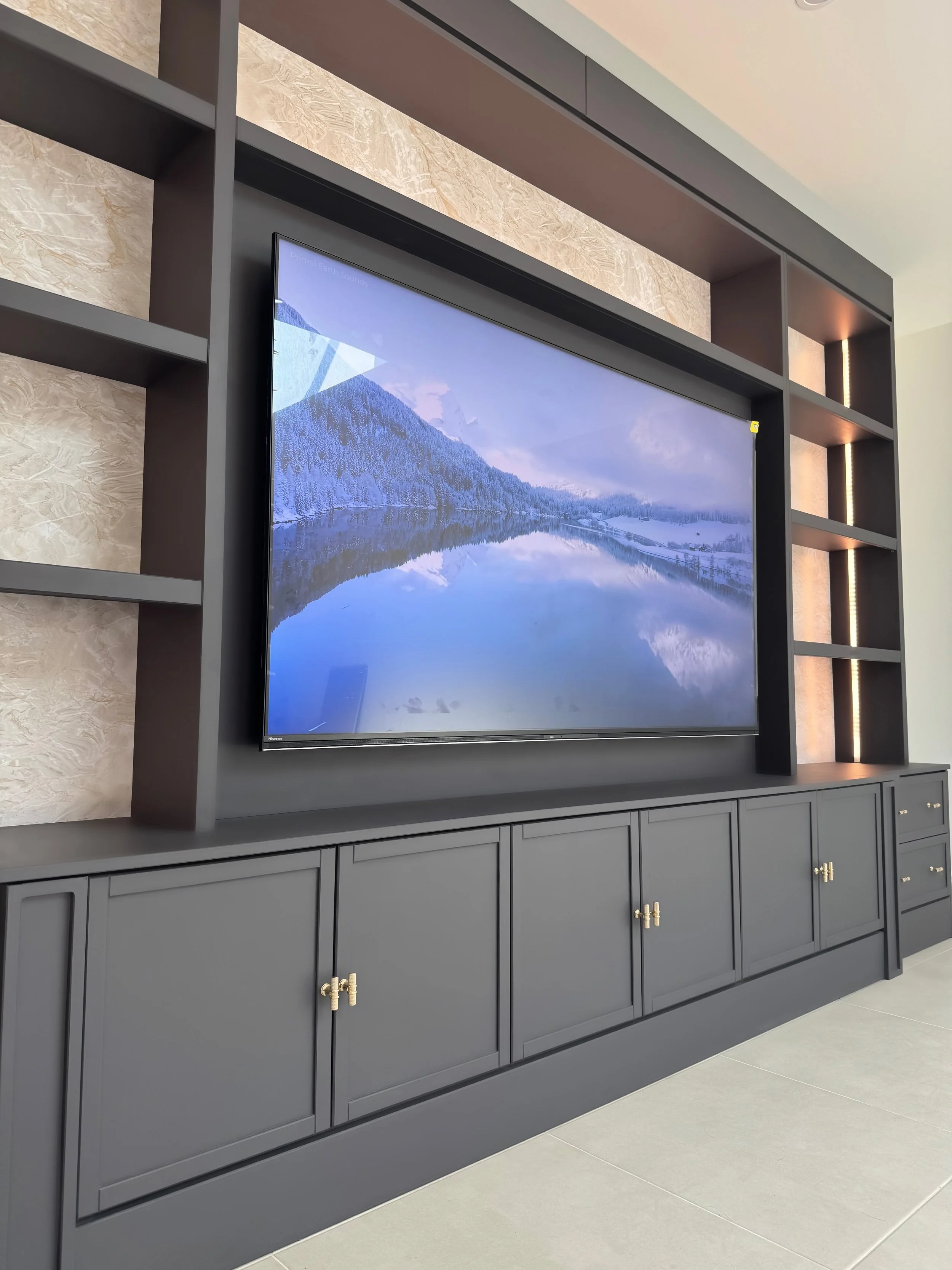 A modern TV unit with a large flat-screen TV mounted on a dark grey cabinet and open shelving, displaying a snowy mountain landscape reflection. Fitted in Hornchurch.