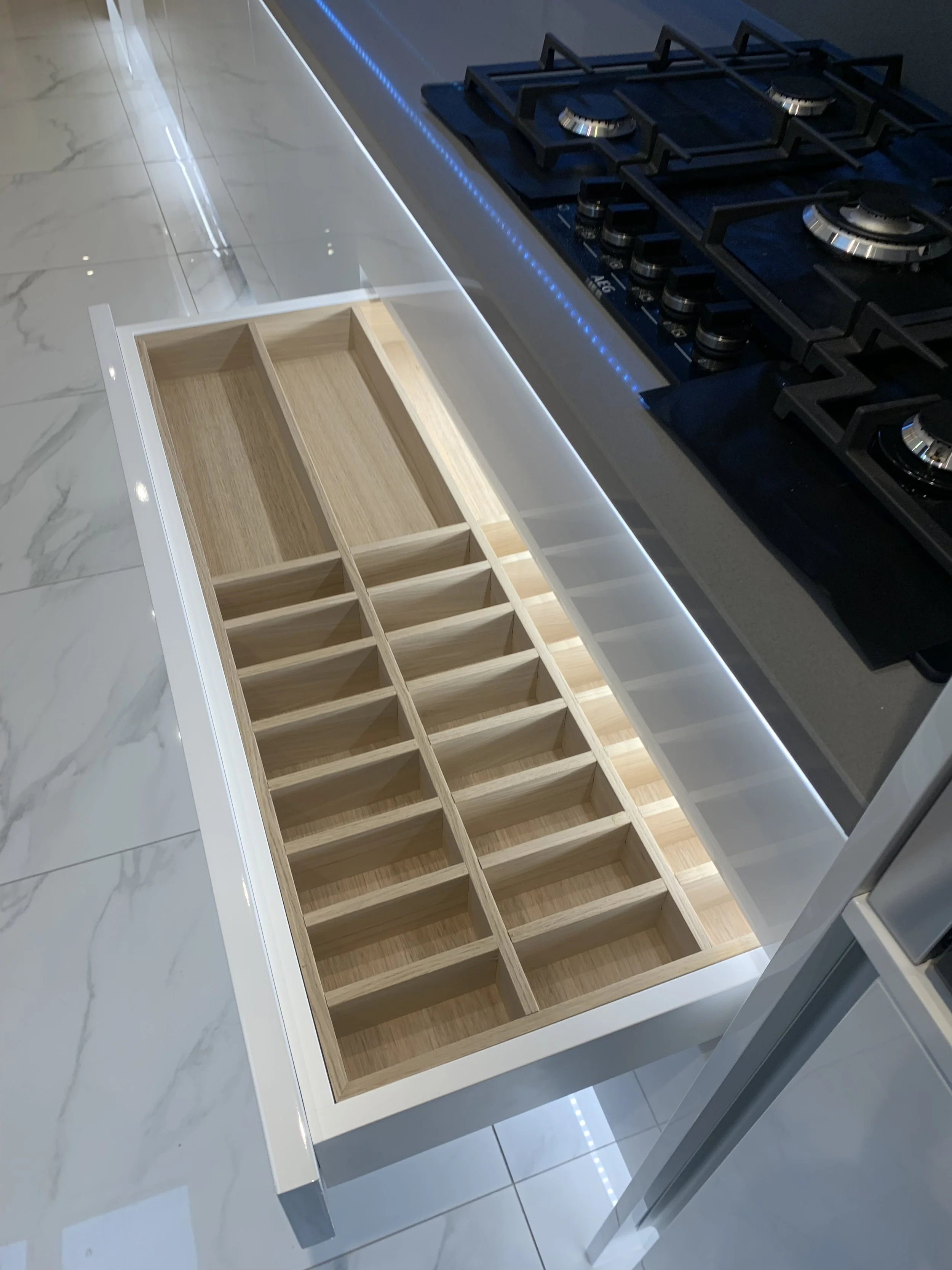 Unfinished wooden drawer organizer on a kitchen countertop next to a black gas stove with blue LED lighting.