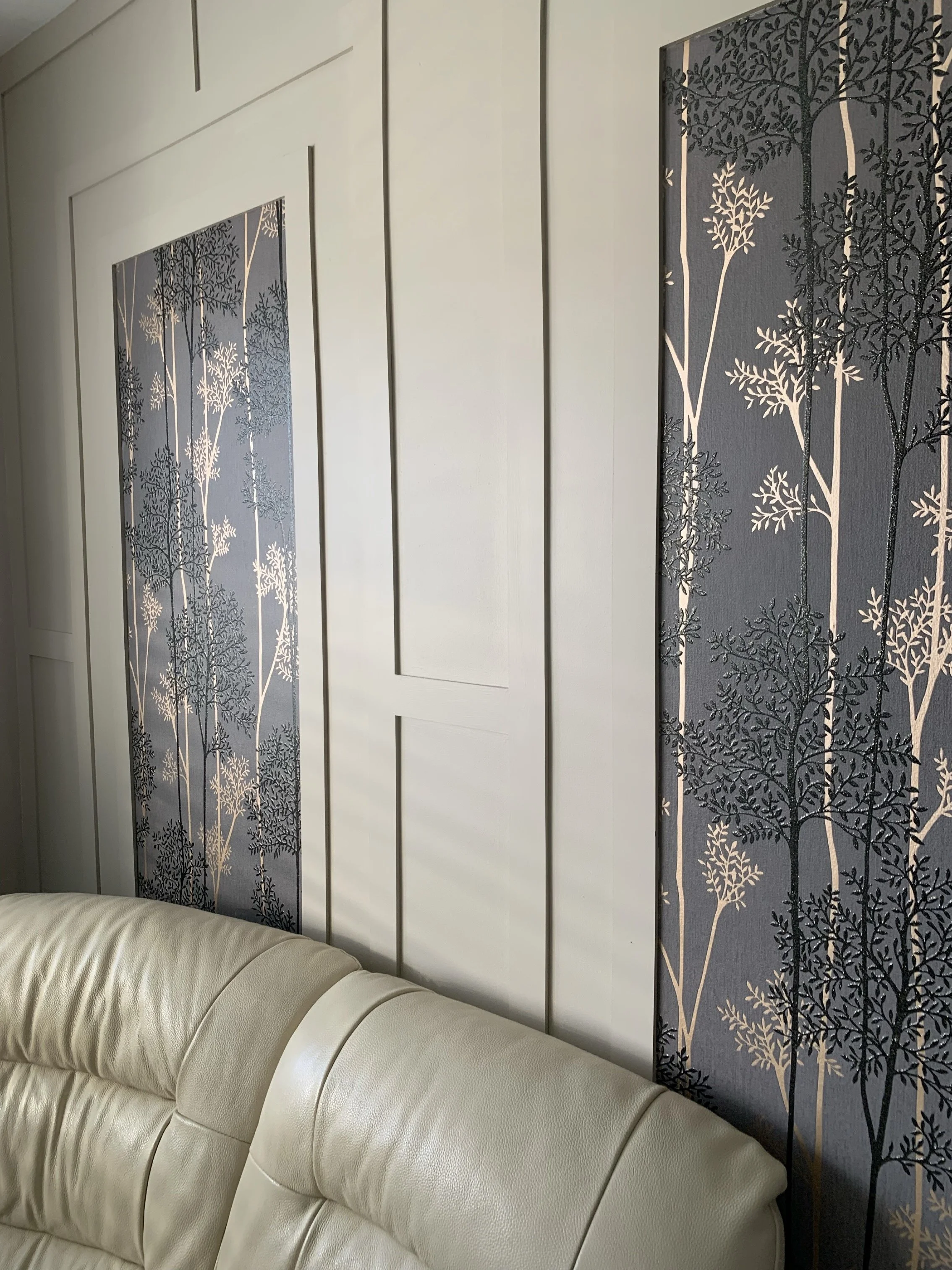 Interior wall with decorative midnight blue panels featuring a white and black tree and foliage pattern, partially obscured beige leather couch in foreground.