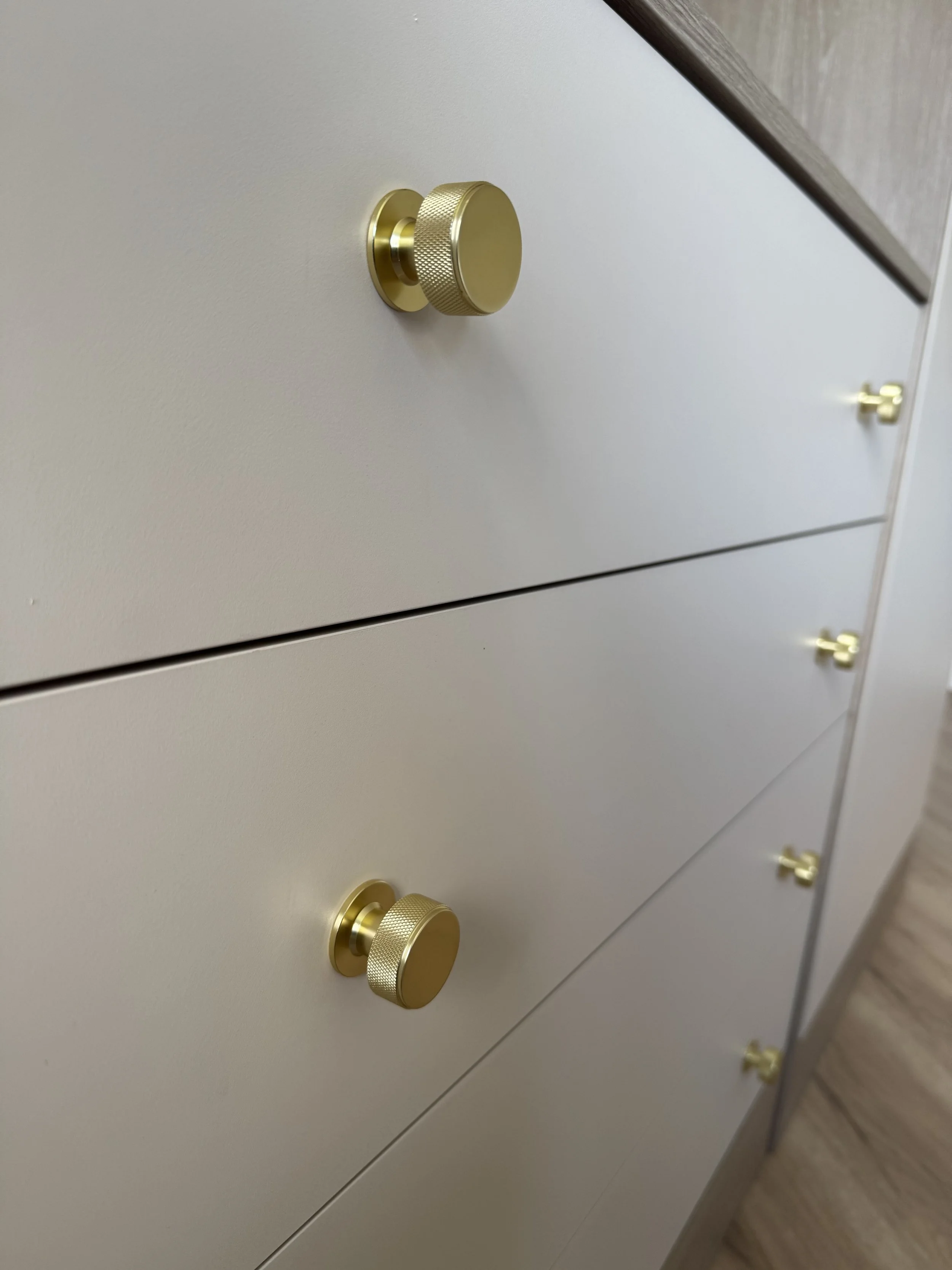 Close-up of a white dresser with gold knobs, angled view showing multiple drawers.