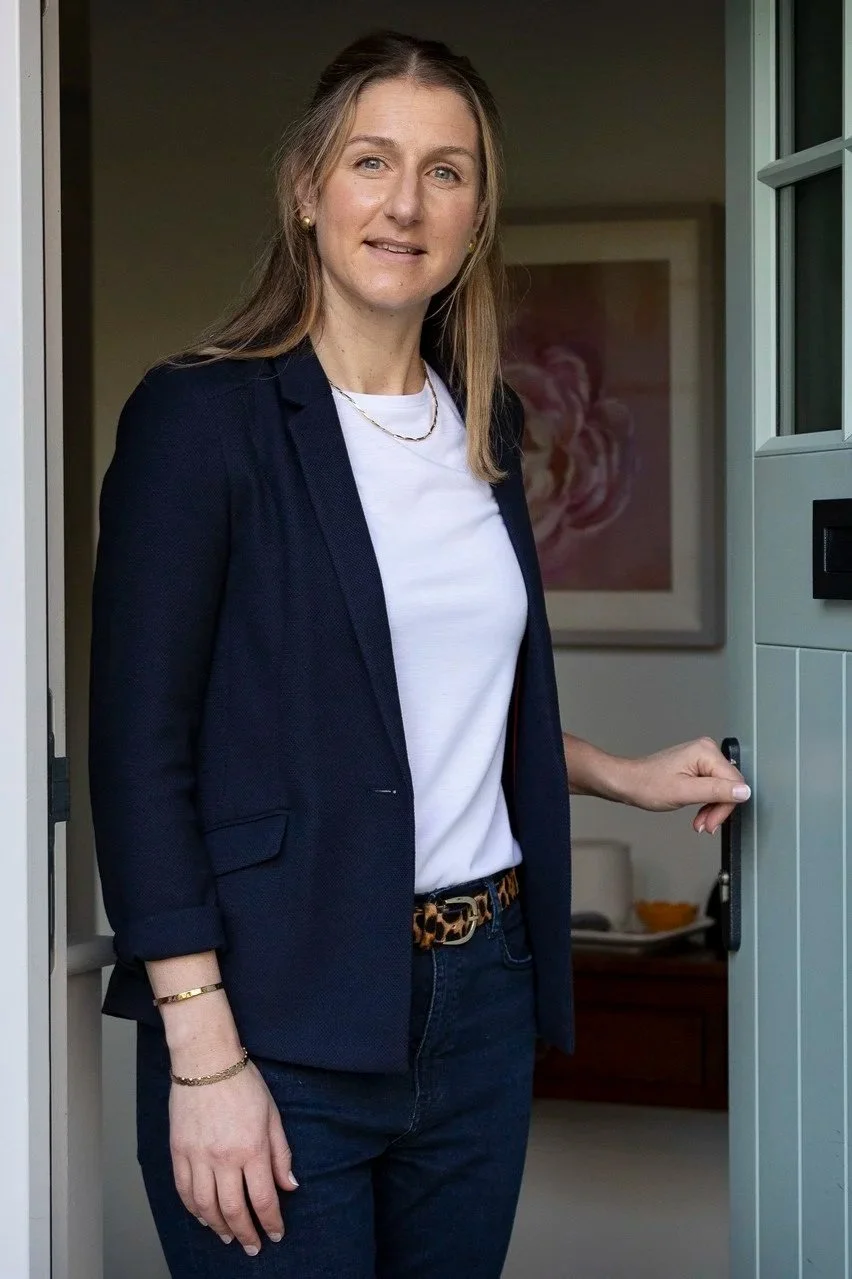 Kirsty Murdoch, professional life coach for mid-career professionals, standing and smiling invitingly by an open door.