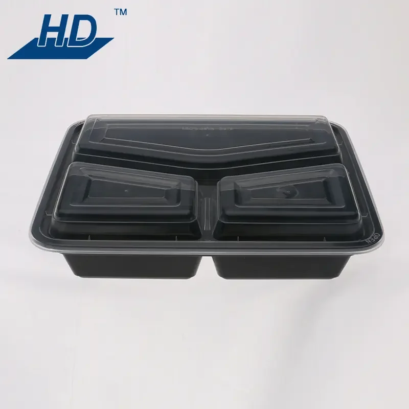A black plastic food container with two compartments and a clear plastic lid, placed on a white surface with an 'HD' logo in the top left corner.