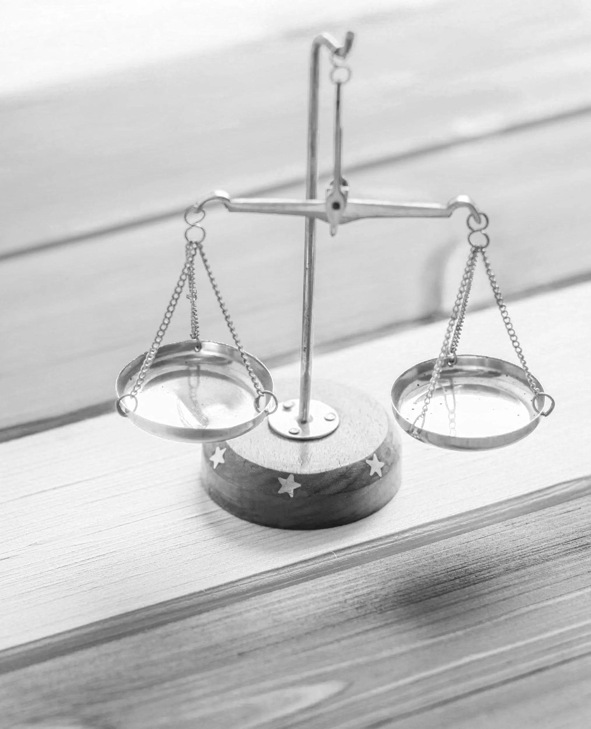 A set of balance scales with empty trays on a wooden surface, with a star decorated base, depicted in a black and white photo.