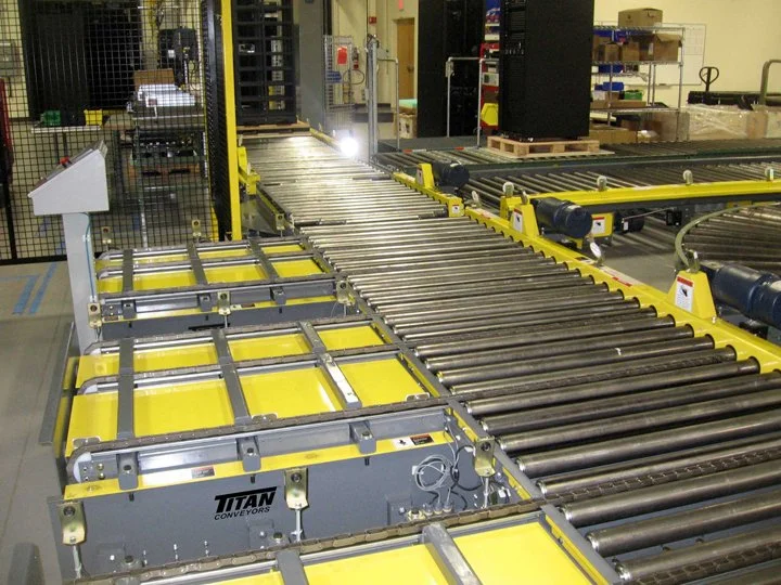 Industrial conveyor system with yellow and gray sections in a warehouse or factory setting.