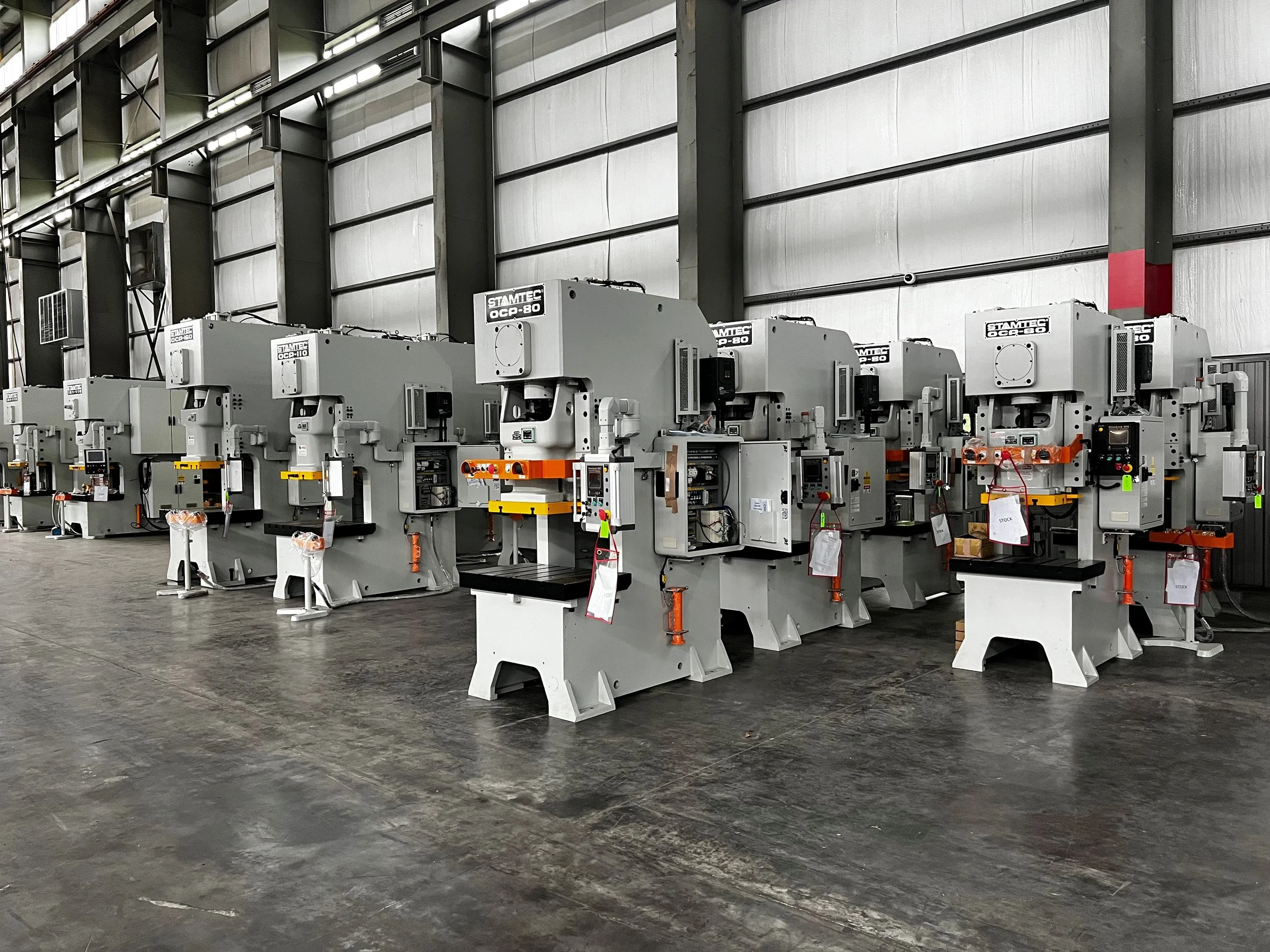 Multiple large industrial CNC machines in a factory, lined up side by side along a concrete floor, with a high ceiling and metal wall panels.
