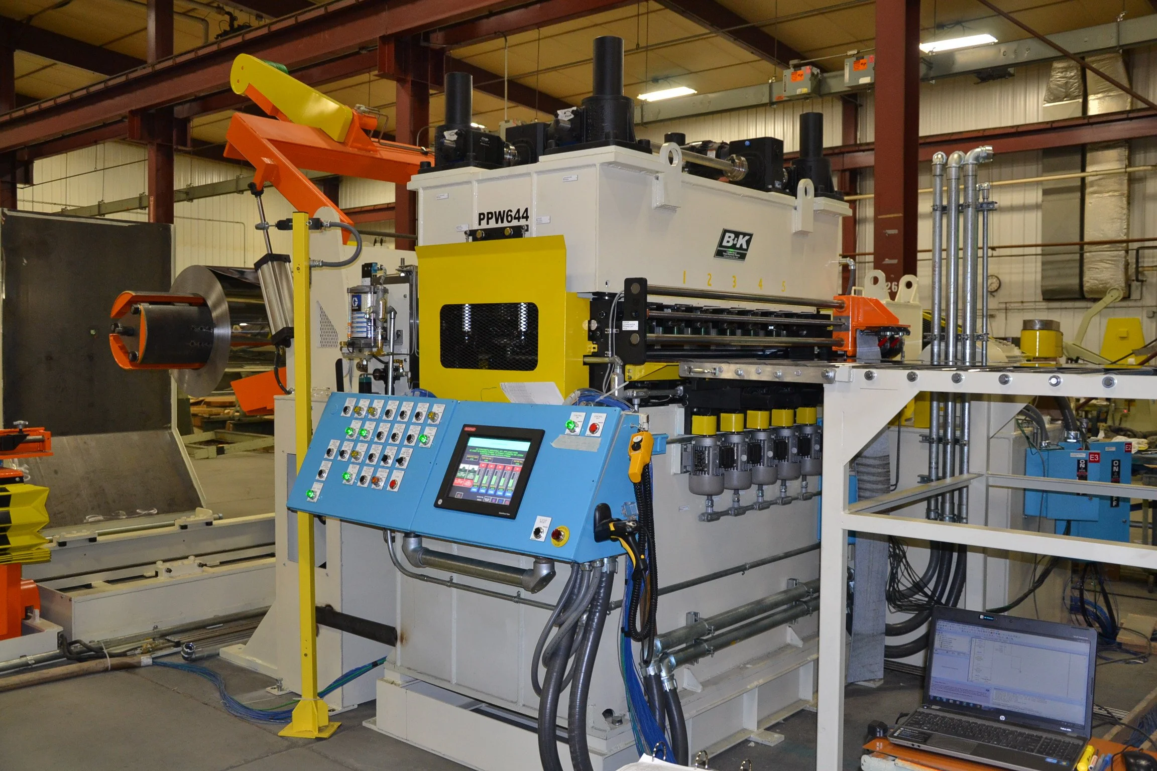 Industrial machine with control panel, pipes, and computer in a factory setting.