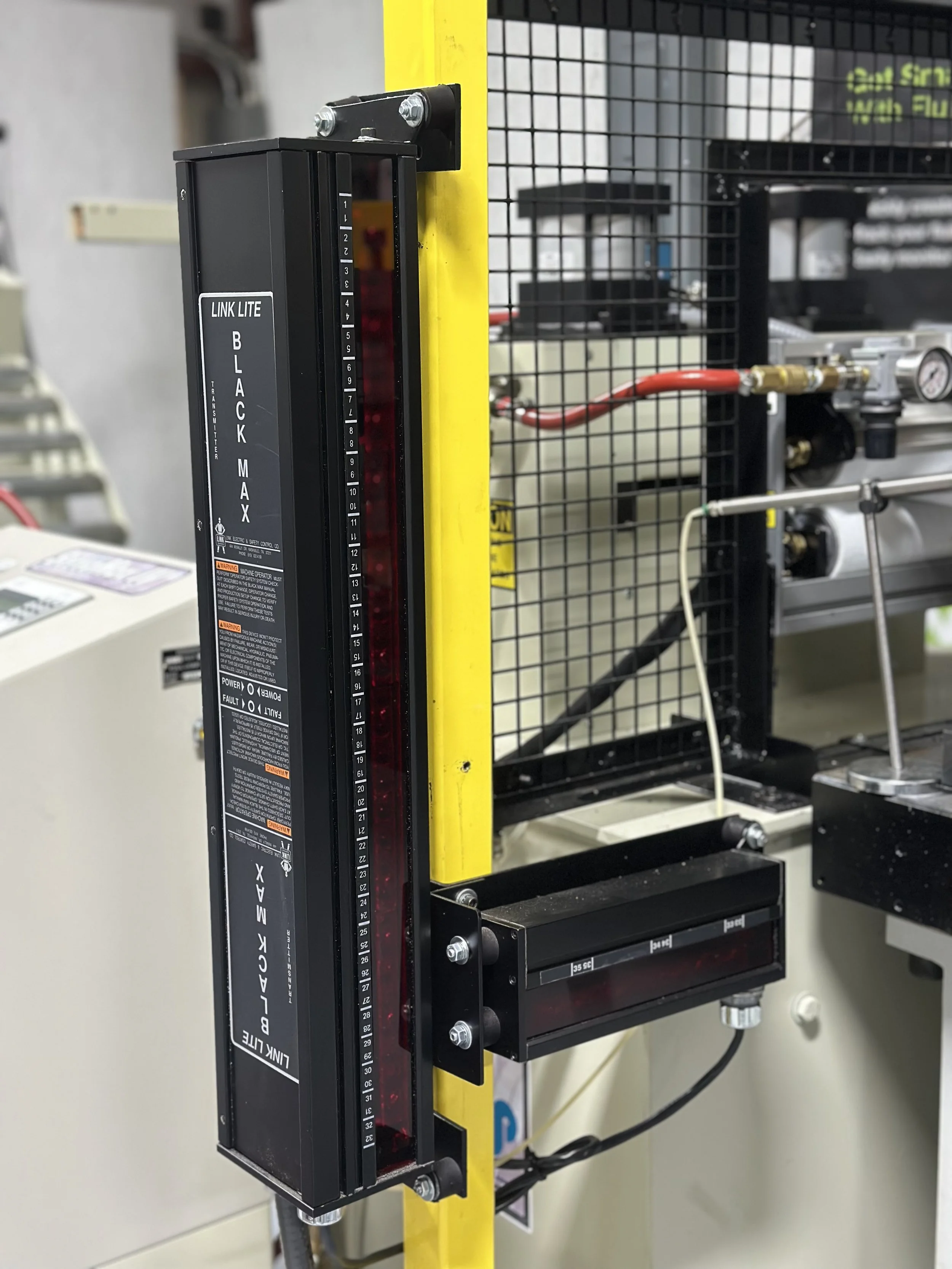 Close-up of a construction laser level device attached to a yellow vertical pole, used to ensure level and precise measurements in construction or engineering work, with various wires and equipment in the background.