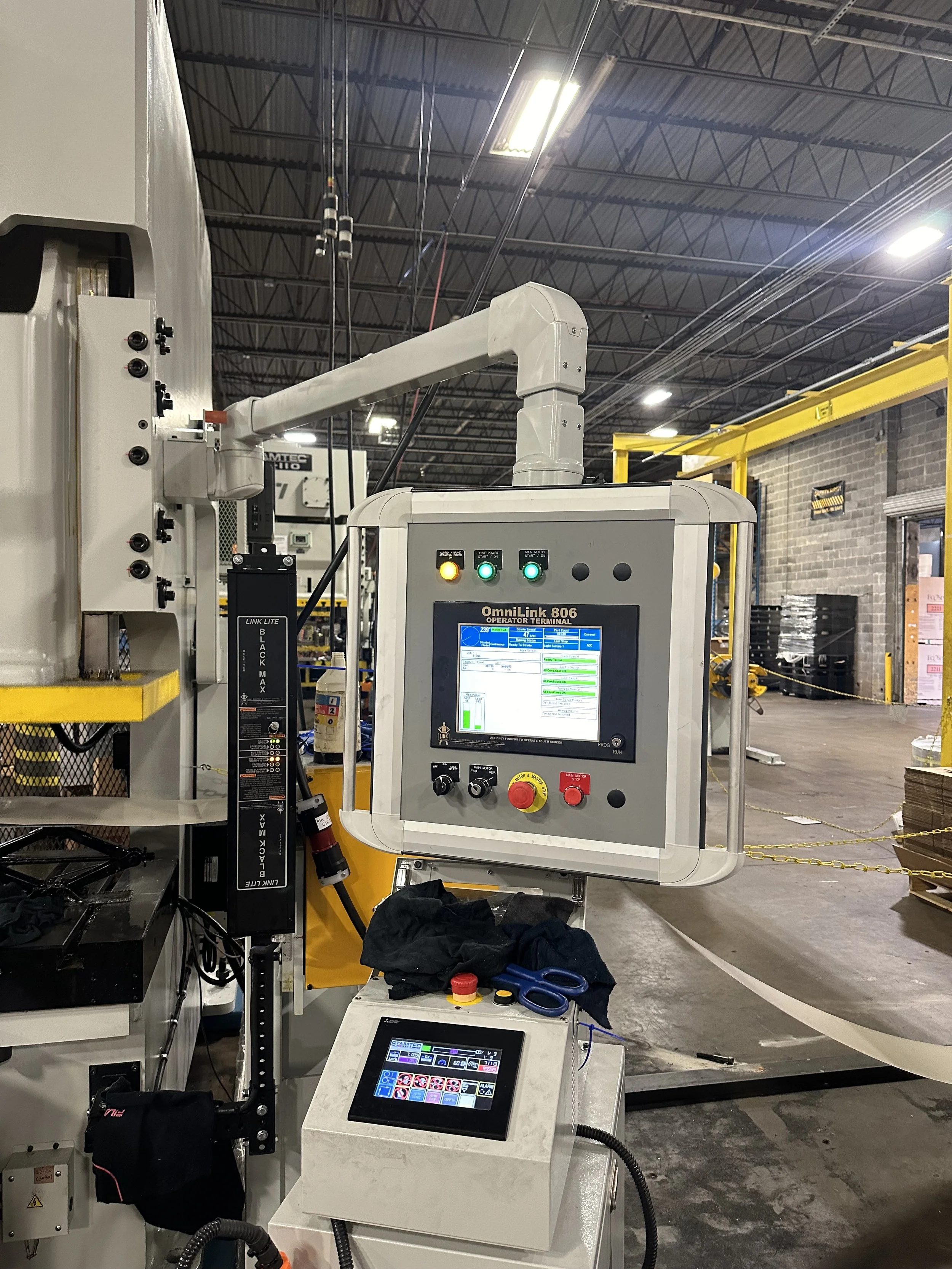 Industrial manufacturing machine with control screens, buttons, and robotic arm in a factory.