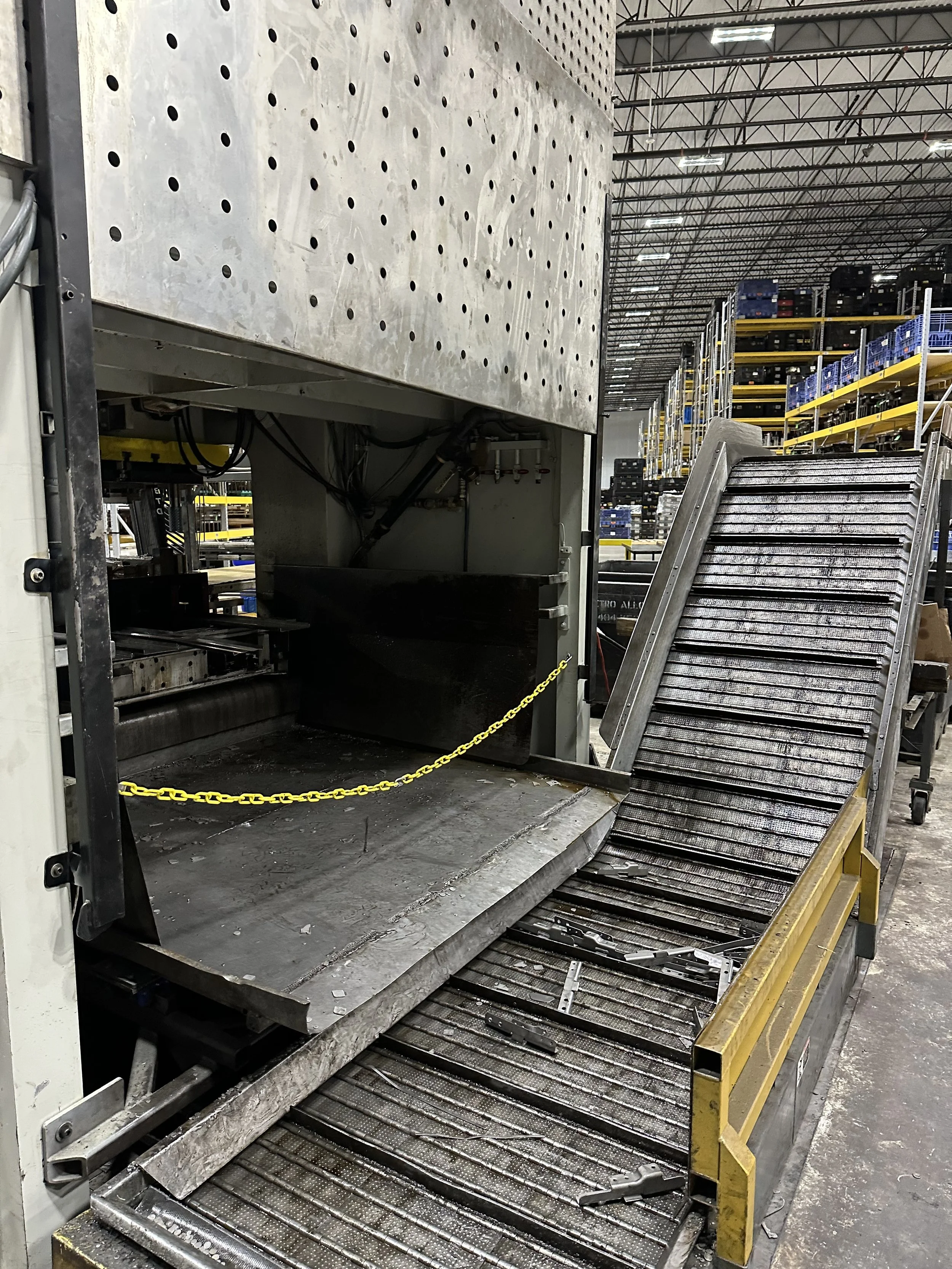 Industrial manufacturing machine with a metal conveyor belt in a warehouse.