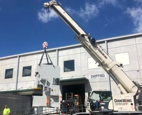 A crane lifting a large piece of equipment outside a shipping facility.