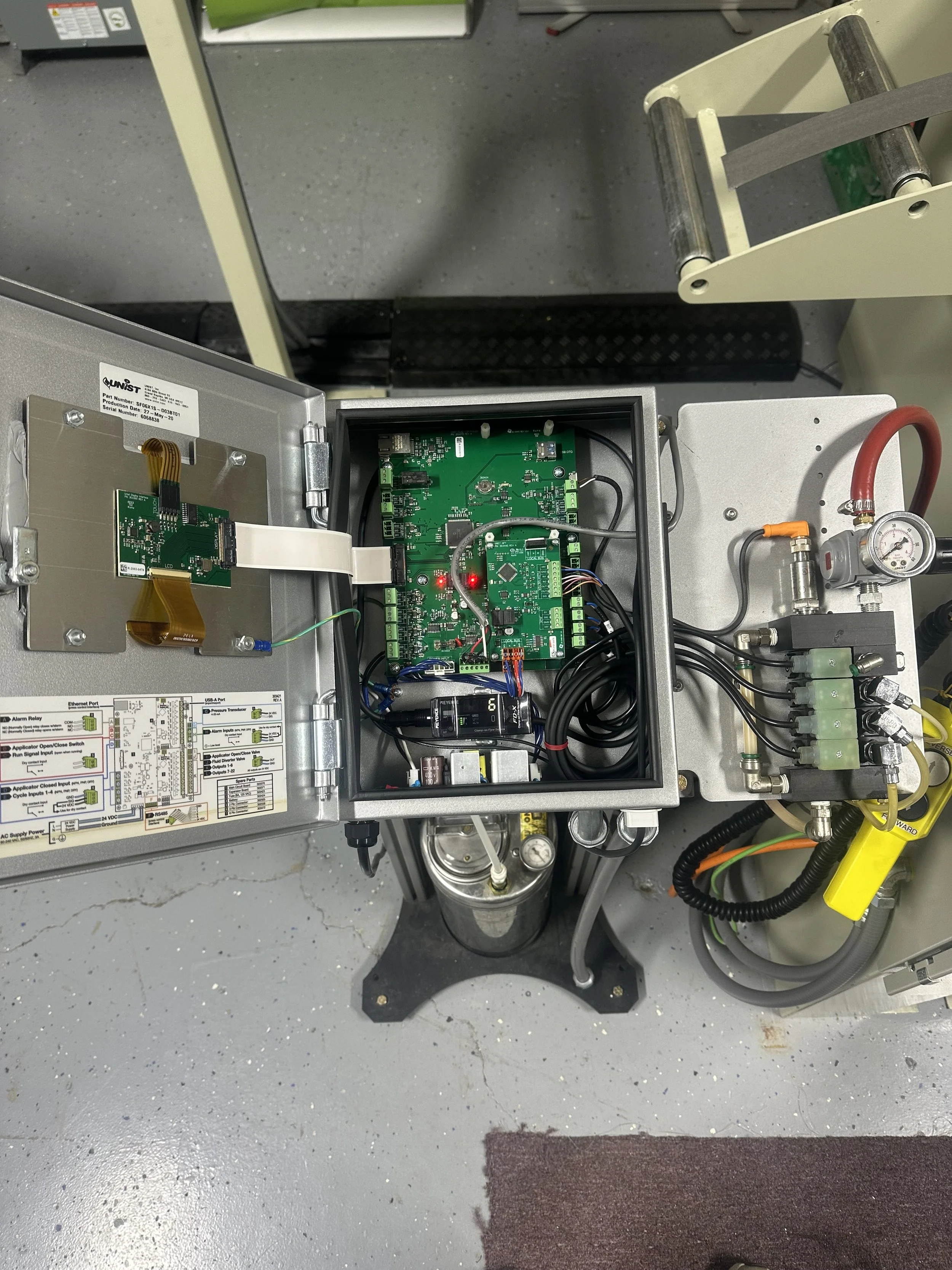 Open electrical control box with various green circuit boards, wires, and electronic components inside, mounted on a metallic surface.
