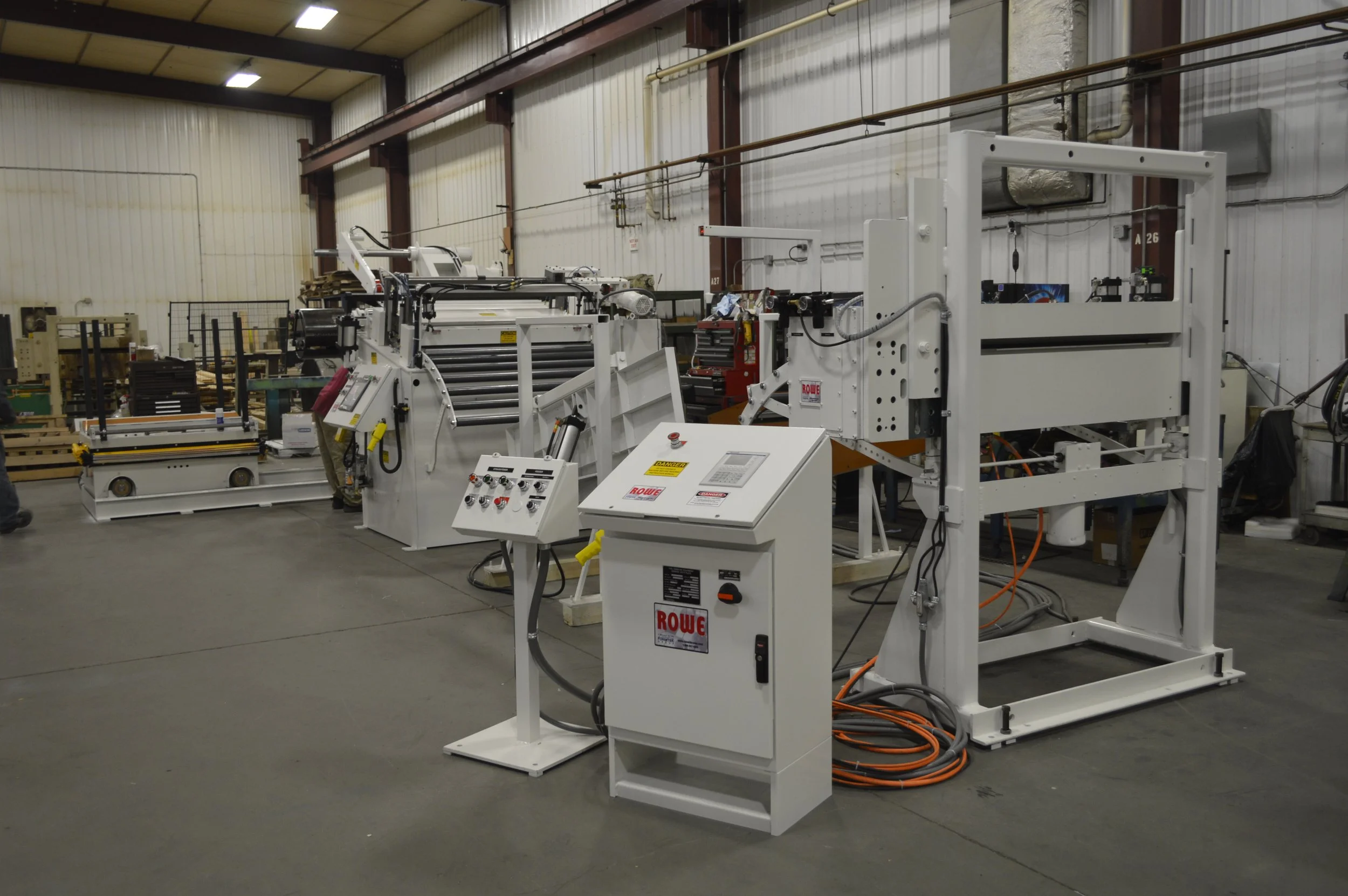 Industrial manufacturing machinery in a warehouse setting with control panels and equipment.