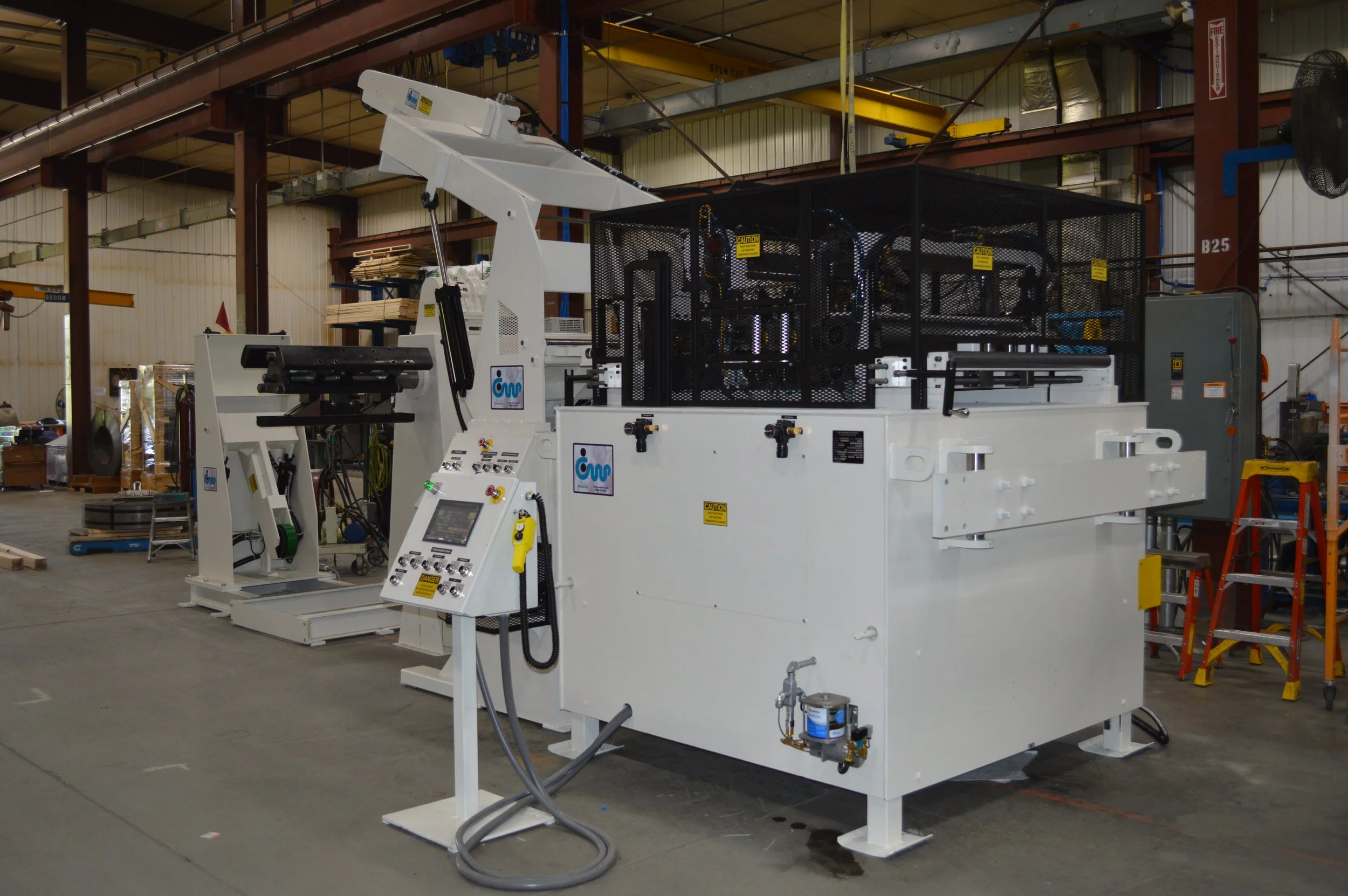 Industrial manufacturing machine in a warehouse with control panels and safety fencing.