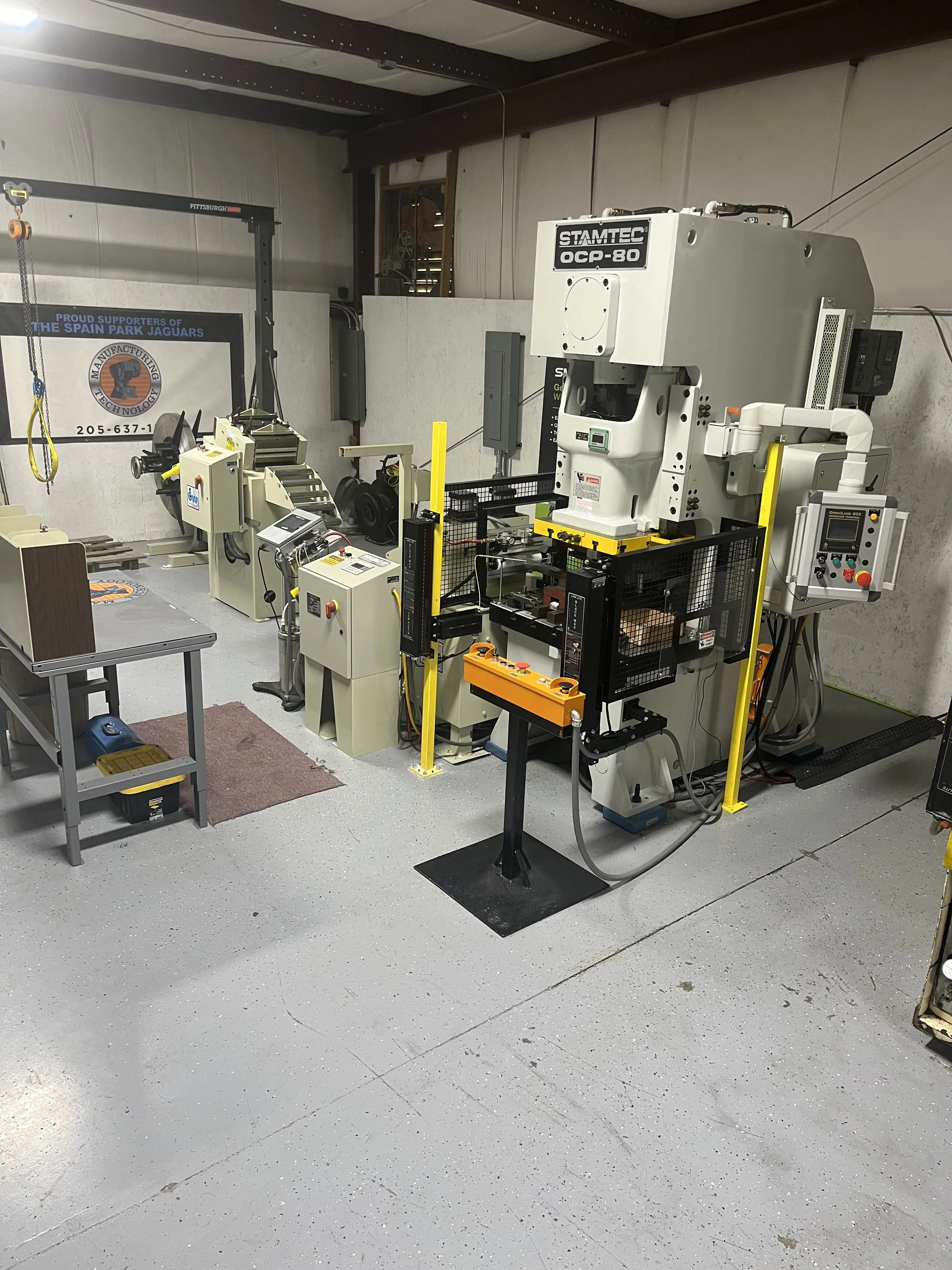 Workshop with large industrial machine and smaller machinery, tools, and work tables, with a banner on the wall supporting the Spain Park Jaguars.