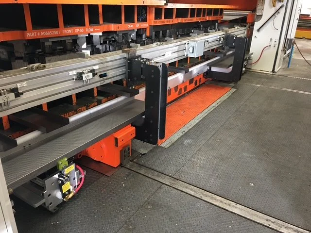 Industrial machine with an orange safety barrier and gray flooring, used for manufacturing or assembly.