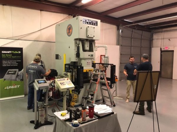 People demonstrating industrial machinery at a trade show or workshop, with equipment and informational displays.