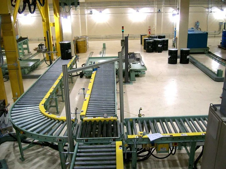 Industrial conveyor system in a warehouse or manufacturing facility with rollers, black bins, and equipment.