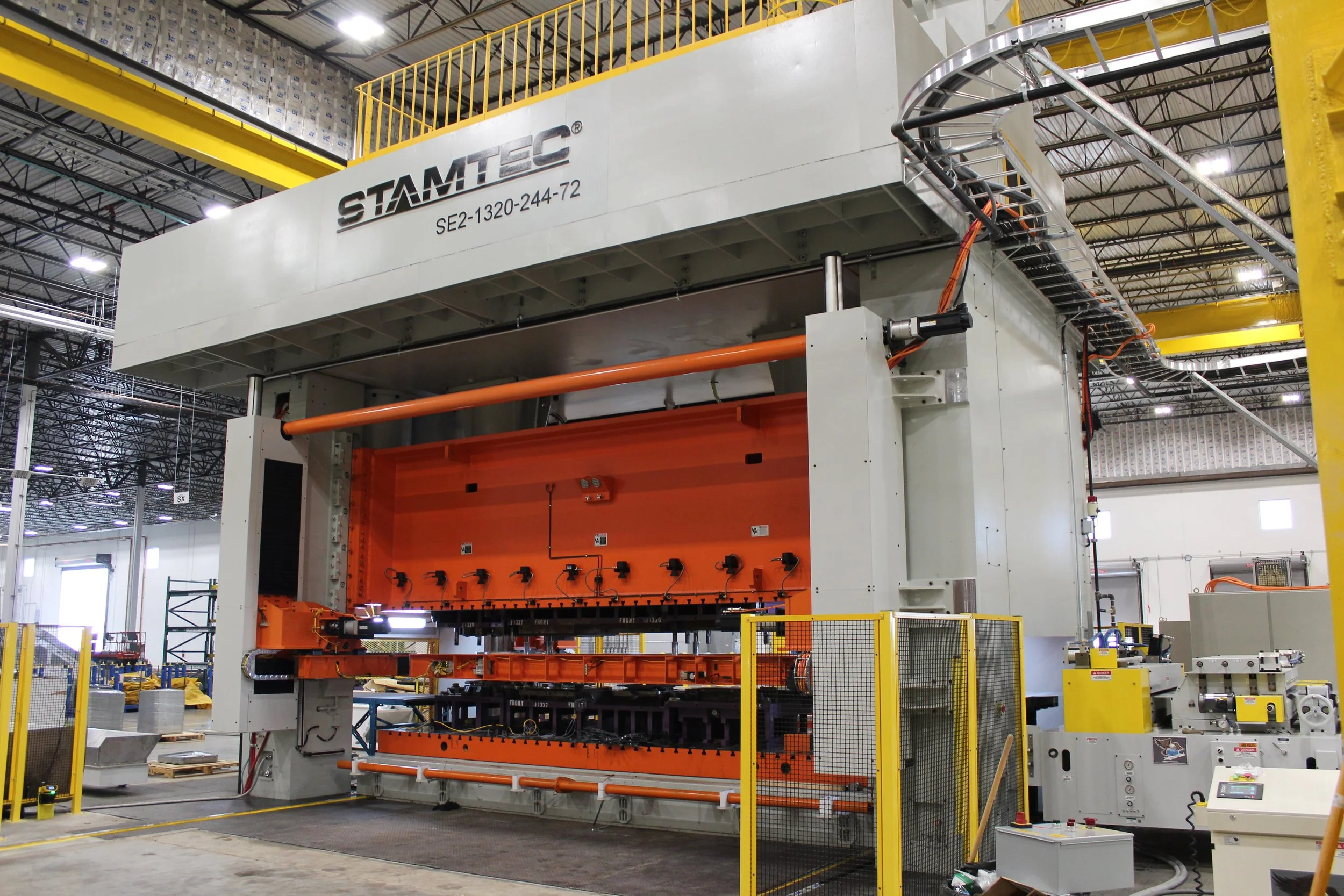 Large industrial machine in a factory with parts and machinery around, marked with the label STAMTEC.