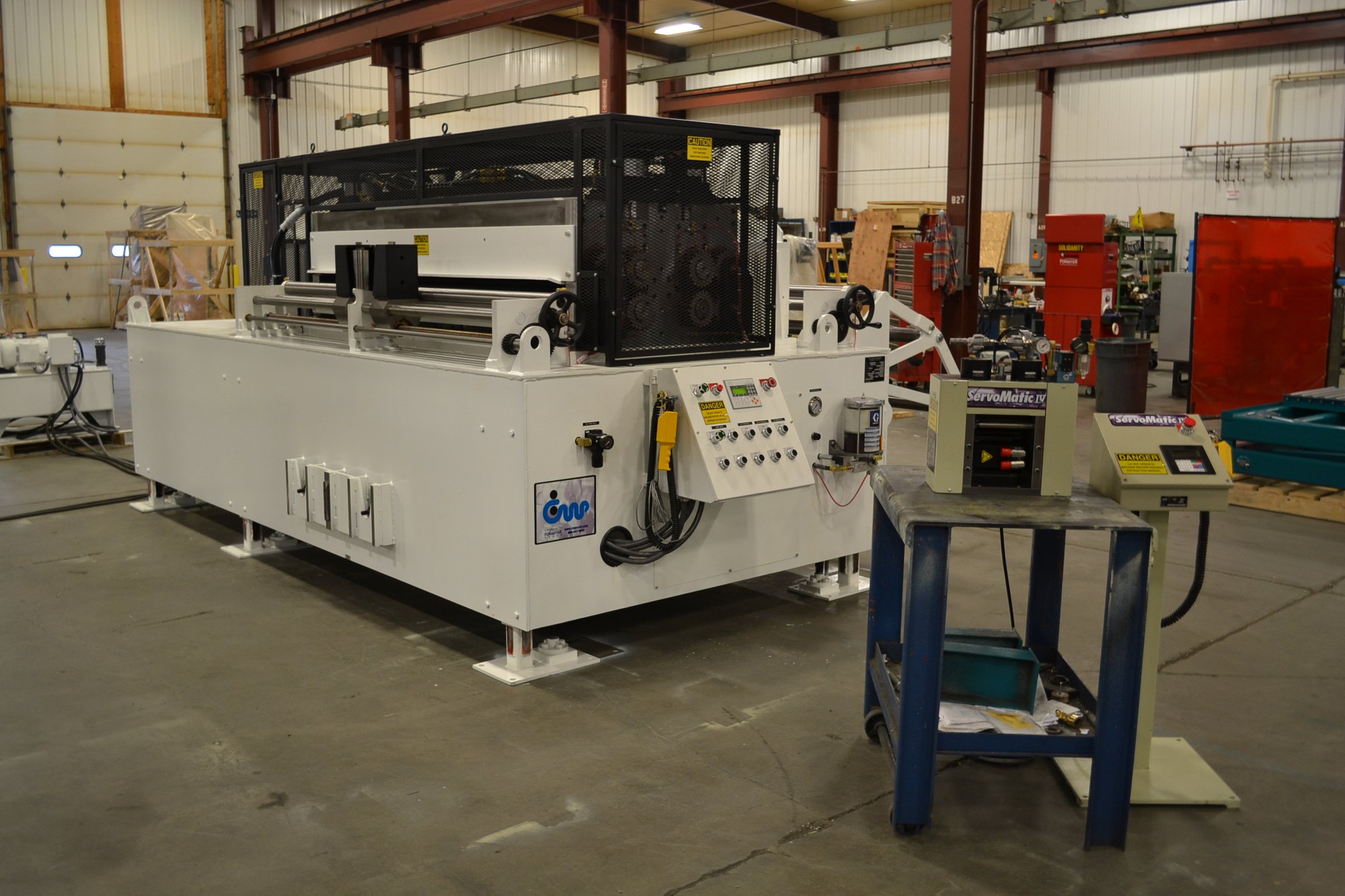 Large industrial laser cutting machine in a warehouse, with control panels and equipment around, used for manufacturing or fabrication processes.