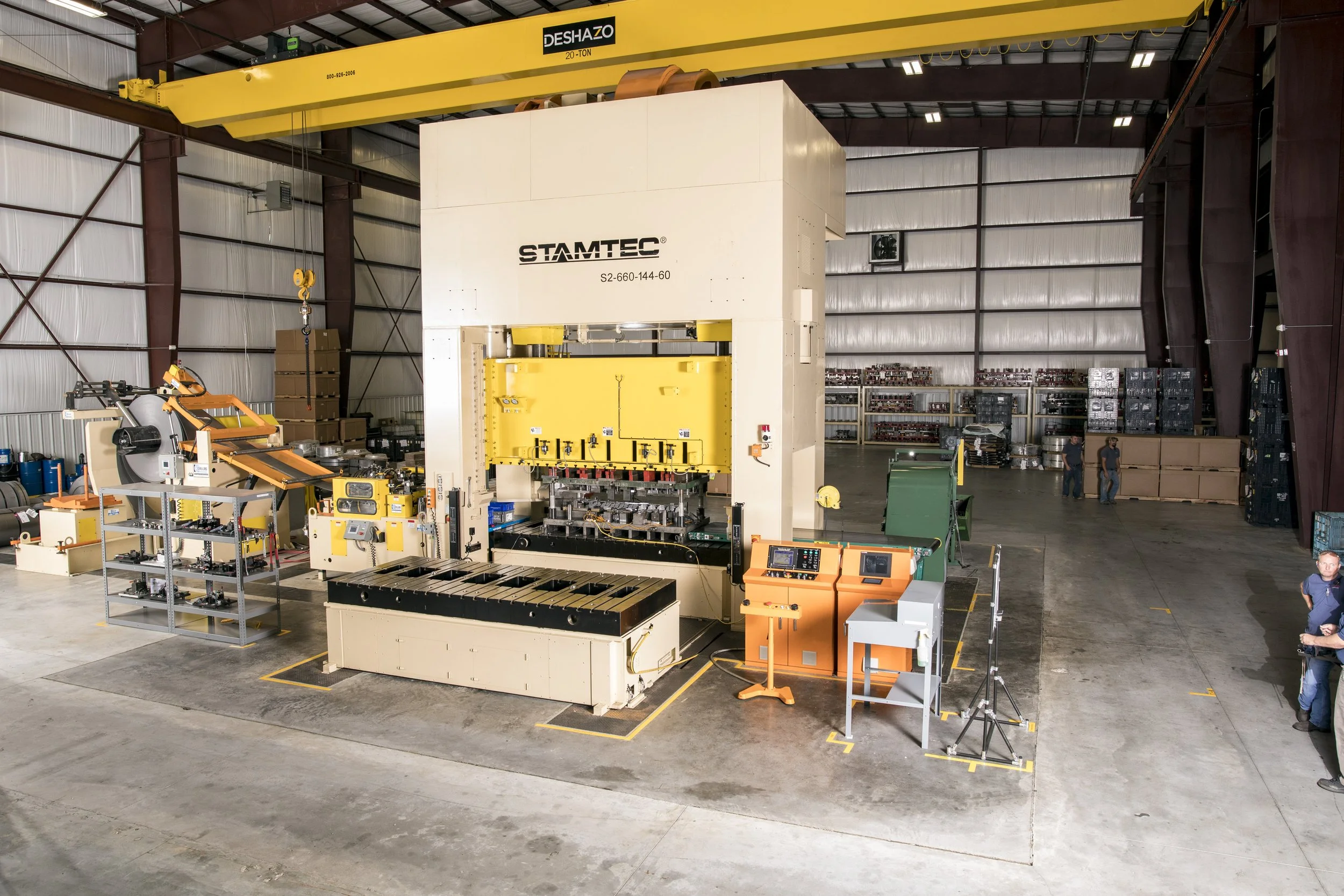 Large industrial manufacturing machine inside a warehouse, with a yellow overhead crane and several workers in the background.