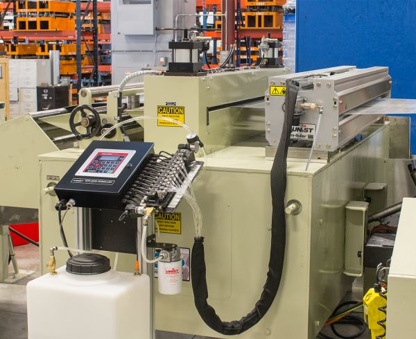 Industrial machinery in a manufacturing setting with control panel, warning labels, and various mechanical parts.